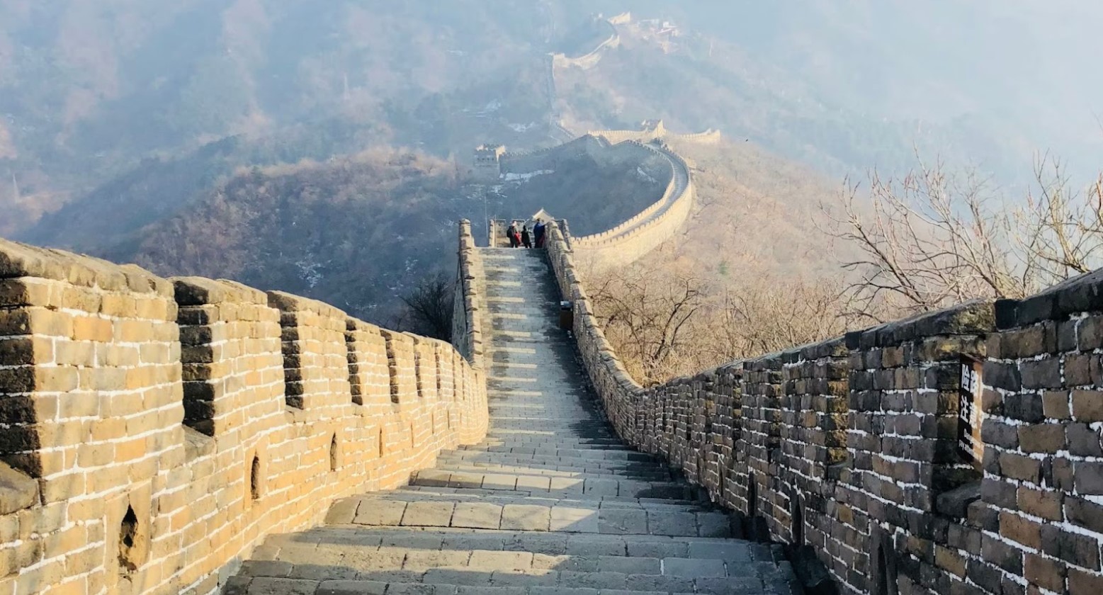 An image from the steps of the Great Wall of China. There are some people on the steps further ahead from where the photo is being taken.