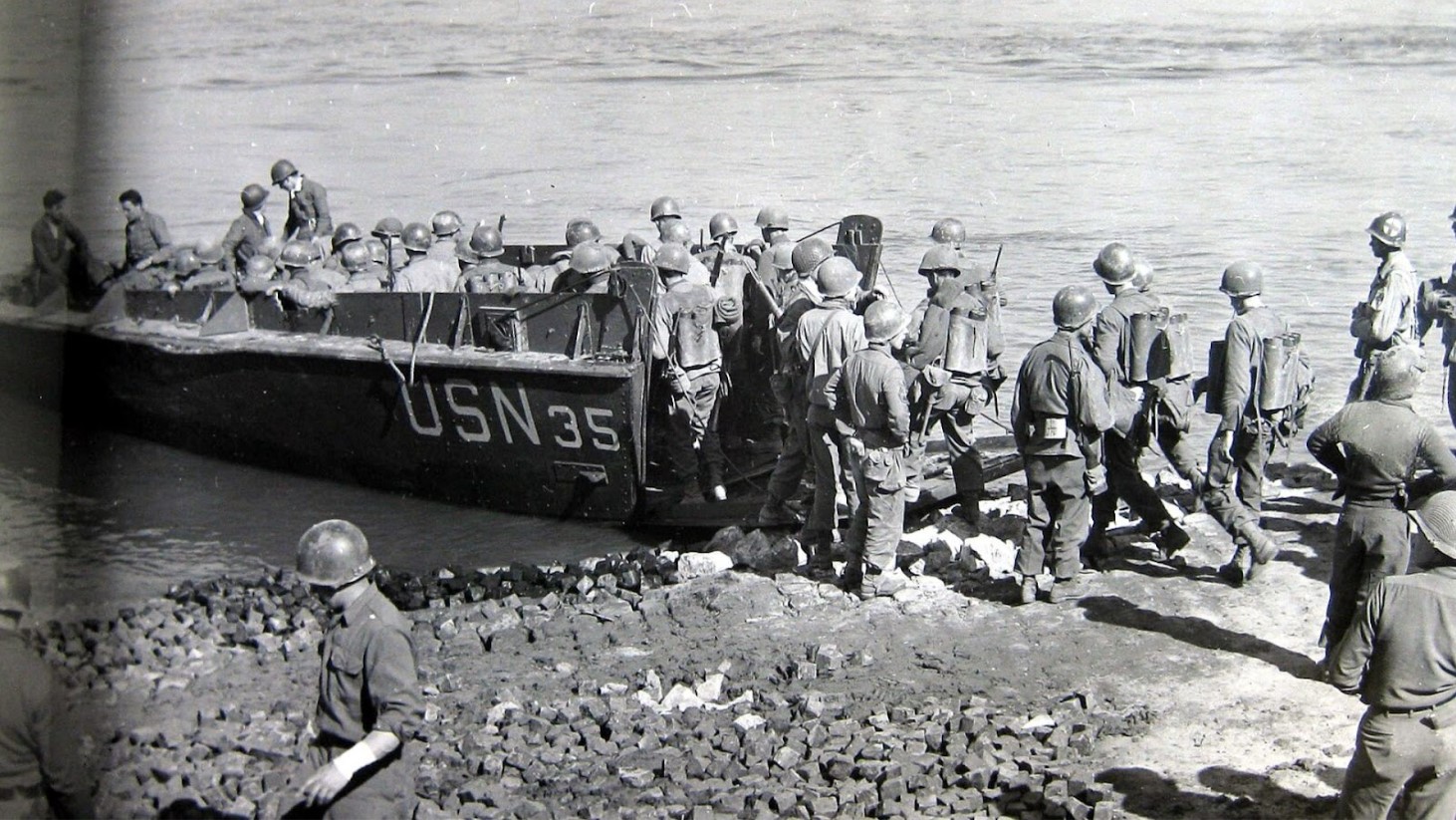 Black and white photograph of soldiers disembarking from a USN (United States Navy) boat numbered 35 onto a rocky shore