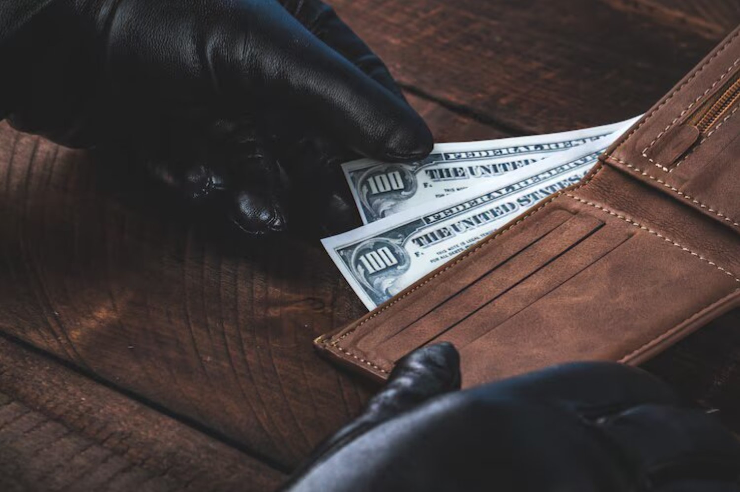 An image of a criminal wearing gloves as he removes $100 bills from his wallet