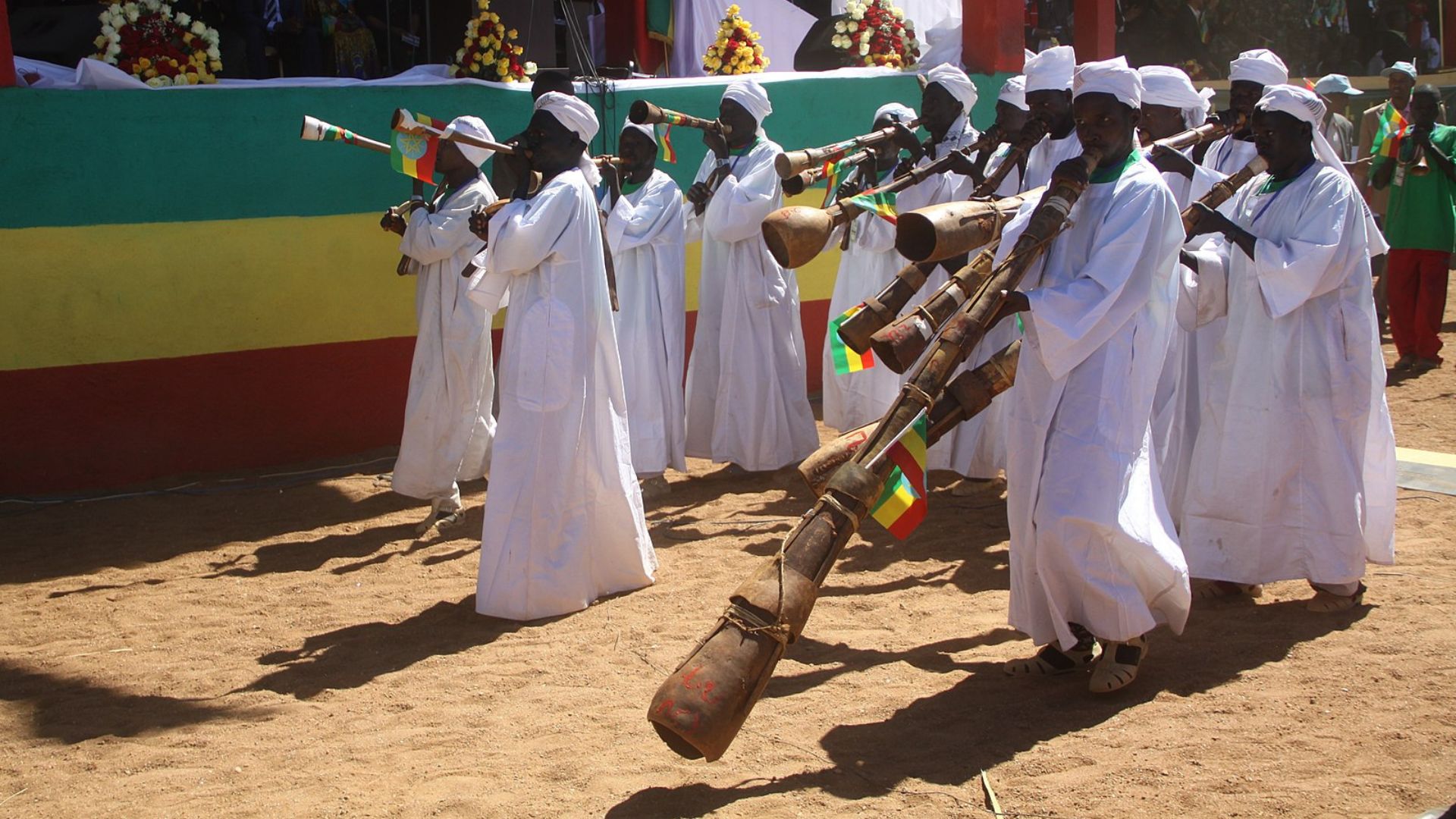 A group of Ethiopian musicians dressed in white traditional clothing and turbans, playing long wooden trumpets at a cultural event