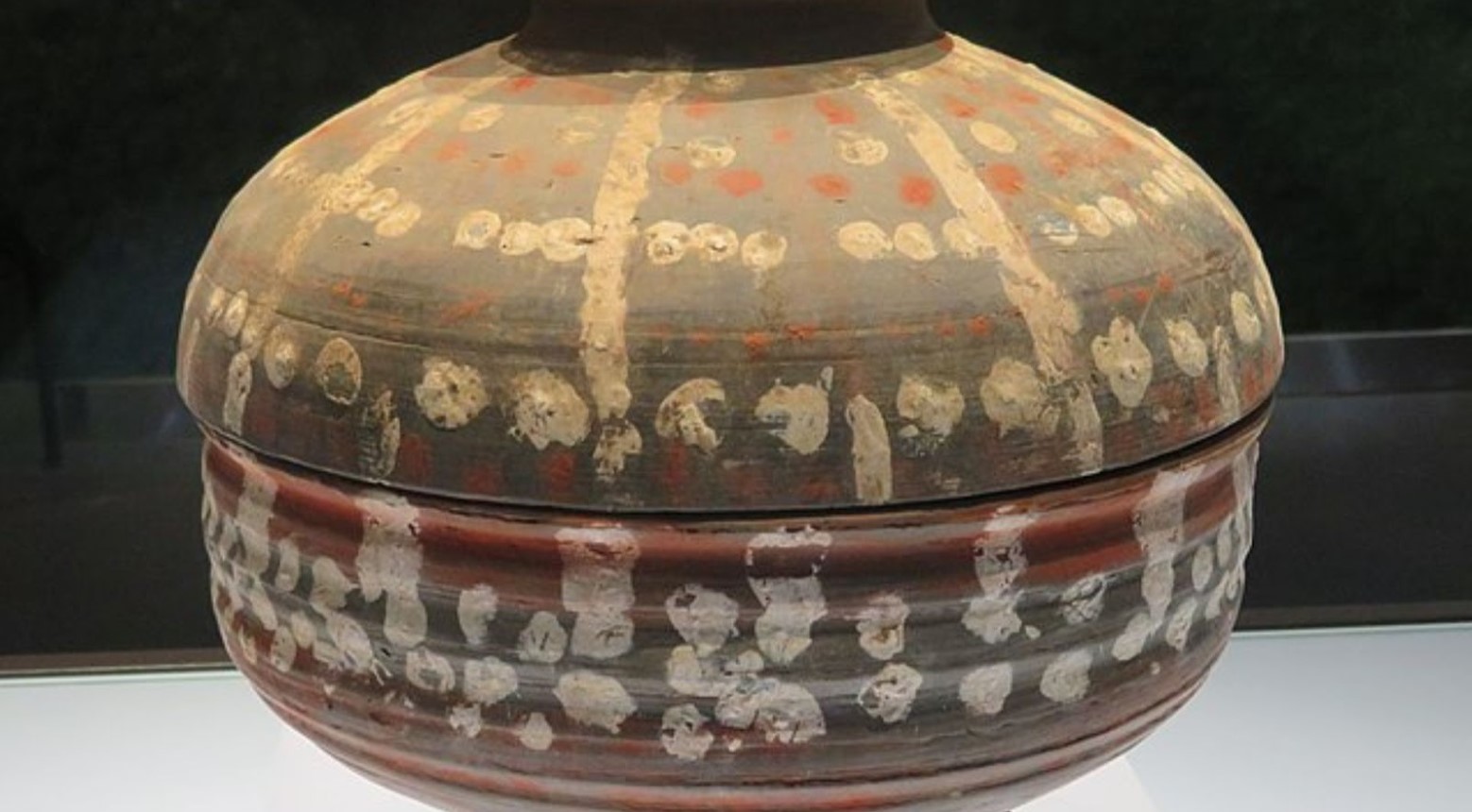 A painted pottery vessel from the Qin Dynasty. The vessel is grey and has red, yellow, and white dots and lines painted on it.