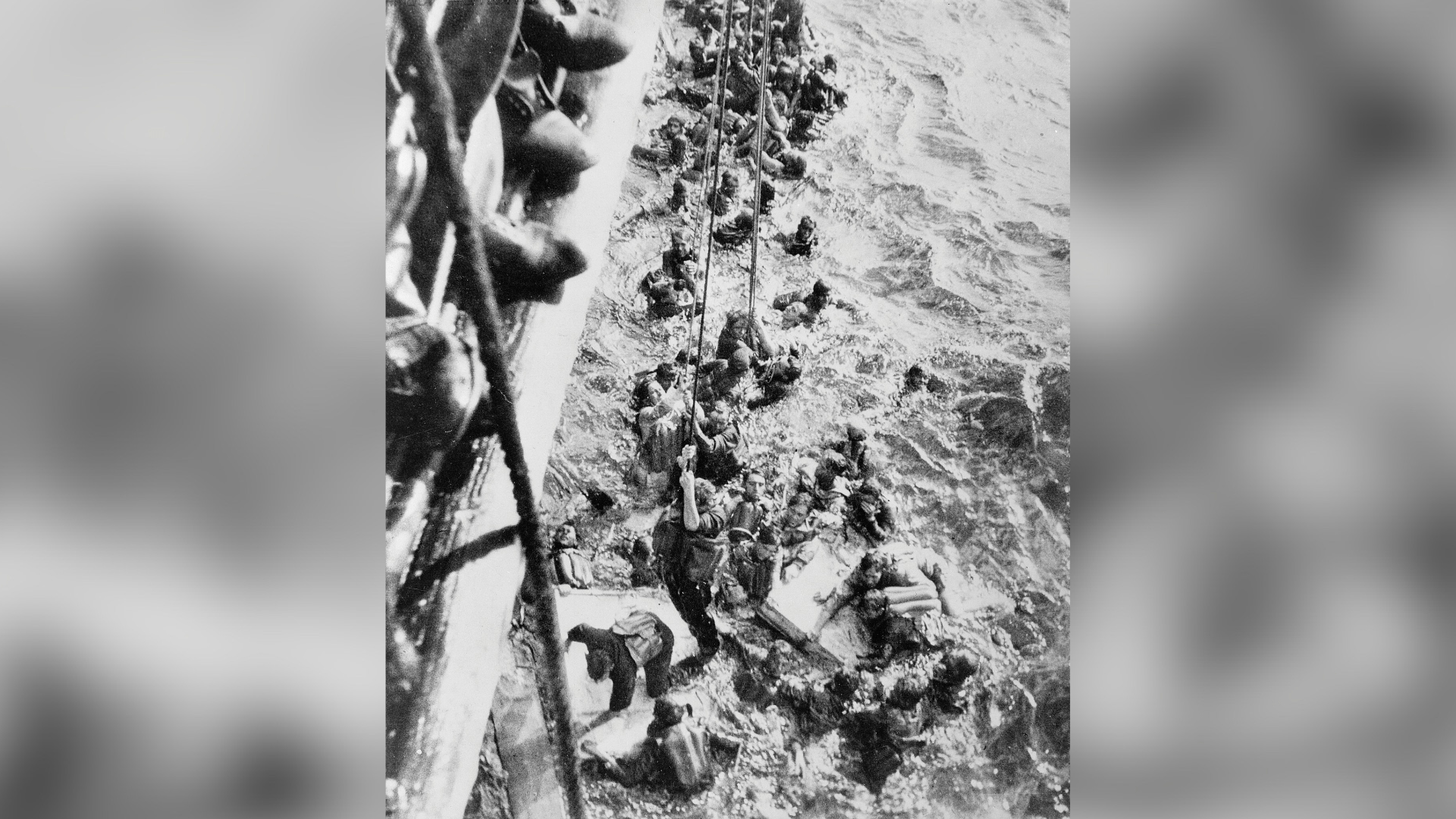 Black-and-white photo of the Dorsetshire crew hosting survivors of the Bismarck out of the Atlantic.