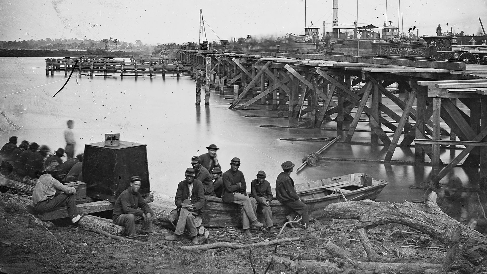 An 1860s Matthew Brady photo of Civil War soldiers sitting on a boat and on the ground near a body of water.