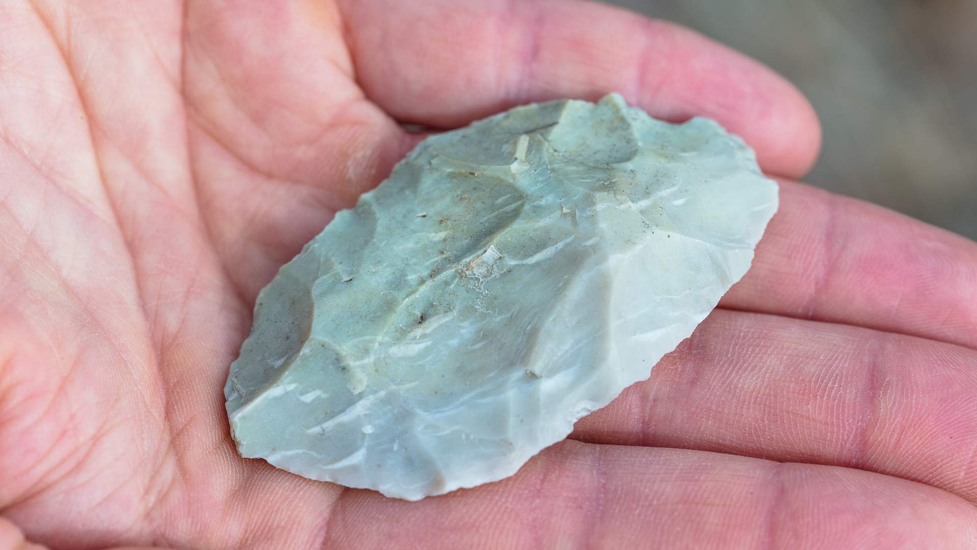 A person holding an ancient chipped stone in their hand.