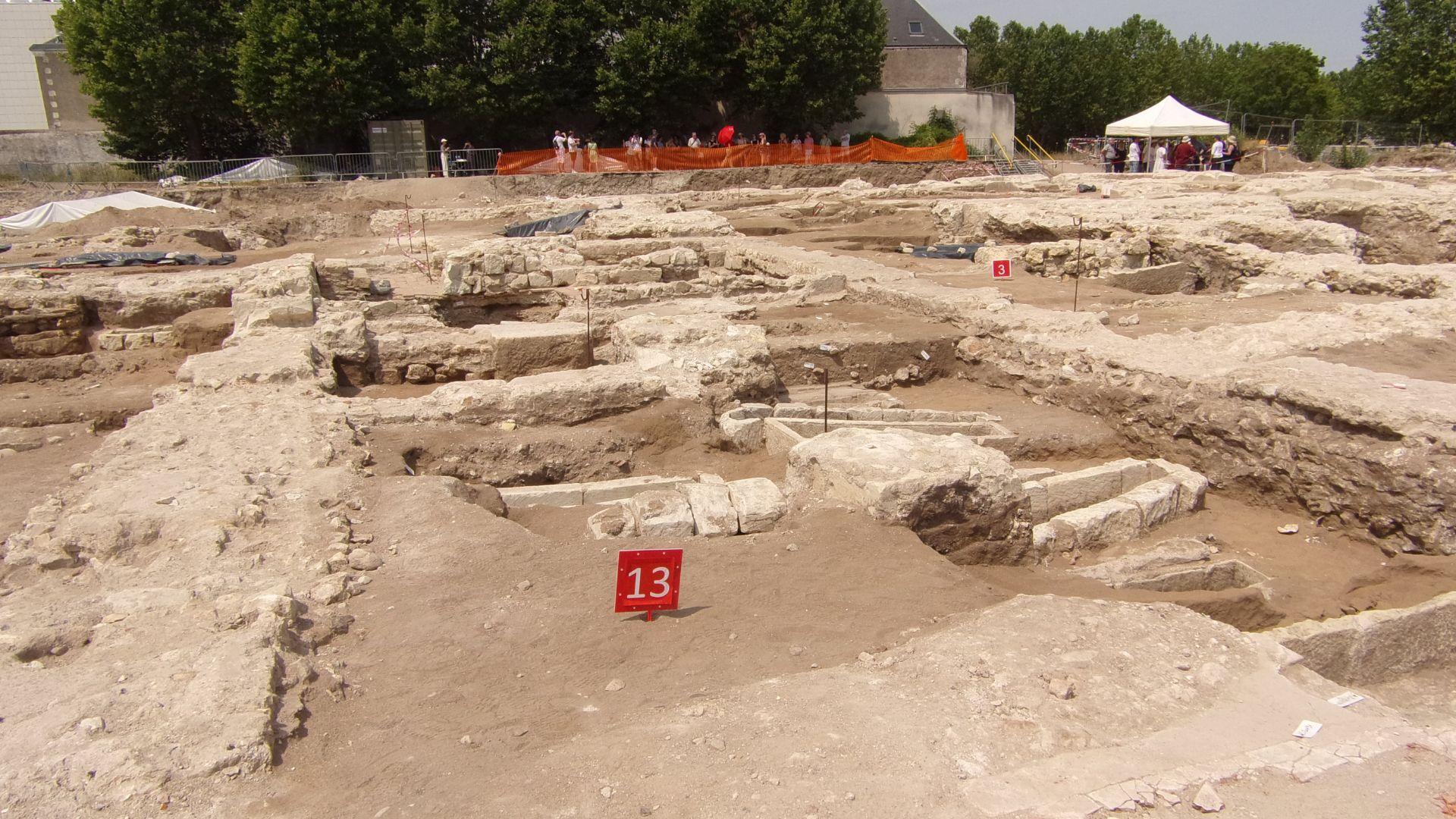 The ruins of Beaumont Abbey’s chapter house, seen during an archeological dig, with people under tents in the background.