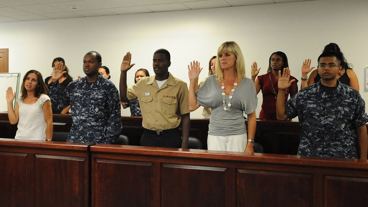 A diverse group of individuals standing in a courtroom, raising their right hands, taking the oath of allegiance during a naturalization ceremony to become U.S. citizens