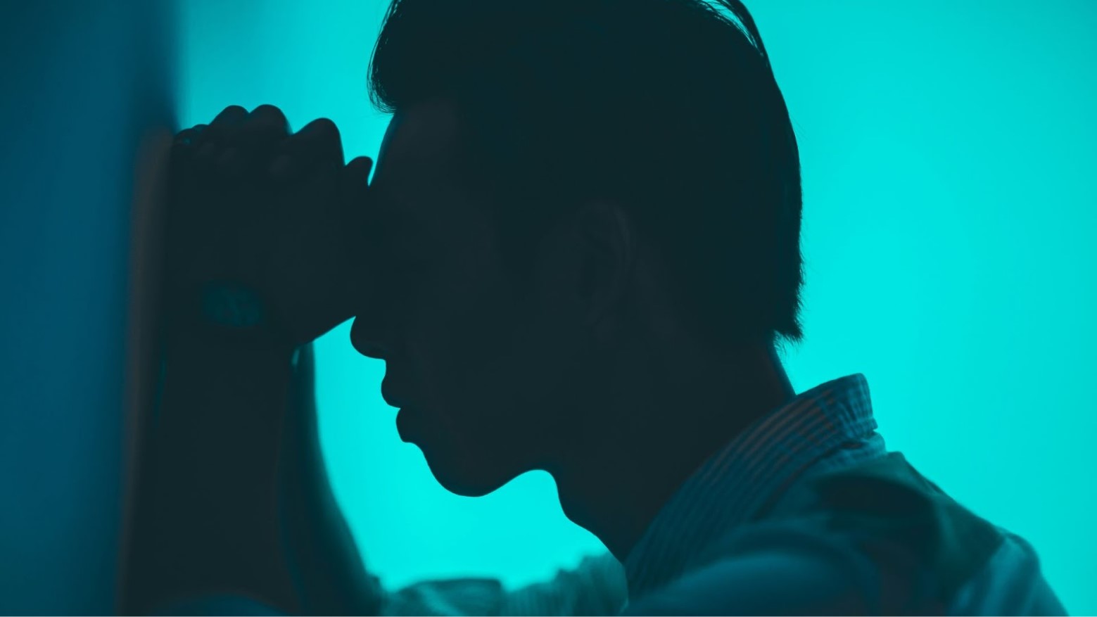 A man putting his hands and head on a wall amid a blue light.