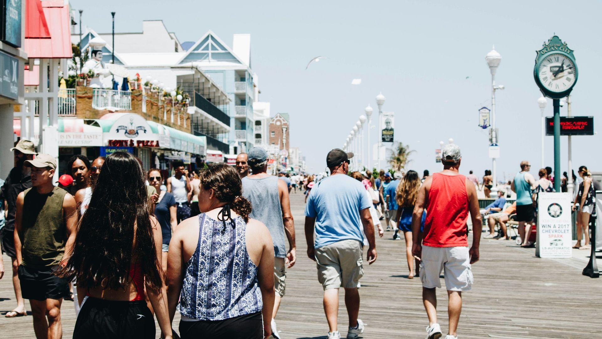 Many people walking on a beach’s boardwalk in the daytime.