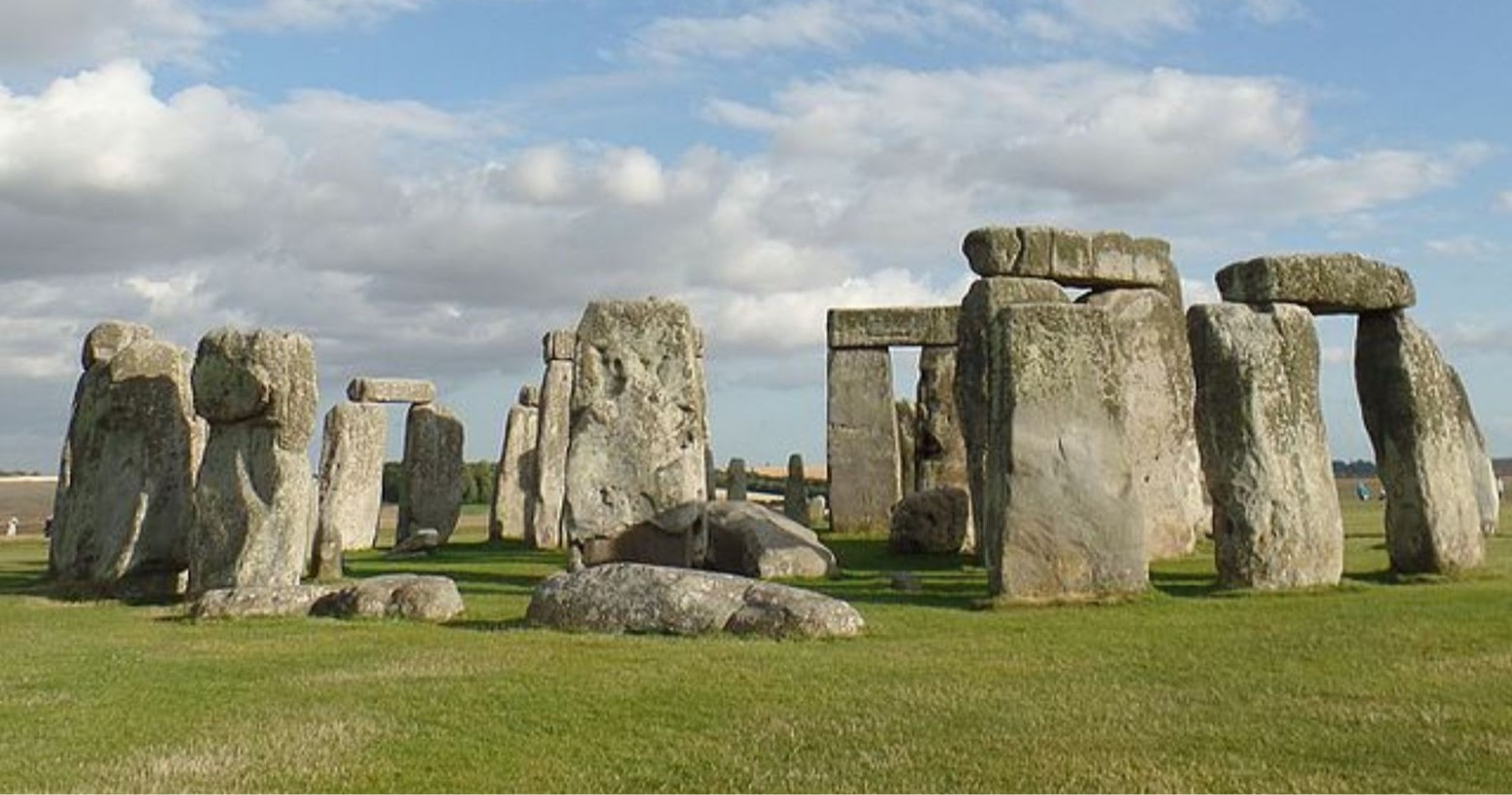 Stonehenge during daytime. There are the main stones that stand vertically, with some laying horizontally on top of them. There are other stones that are lying down on the grass, which are smaller than those standing.