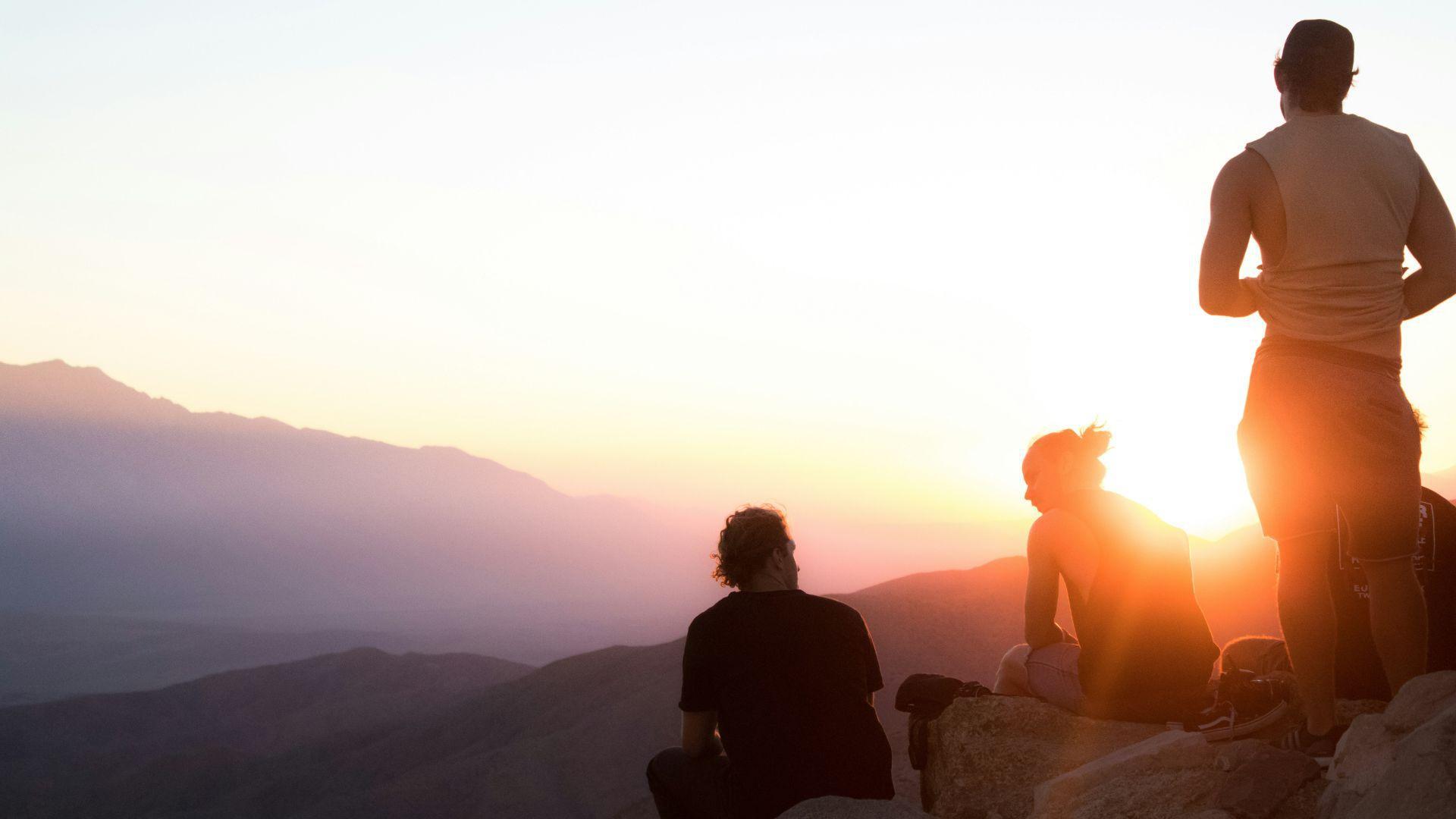 The silhouettes of three men hanging out together in Joshua Tree during a sunset.