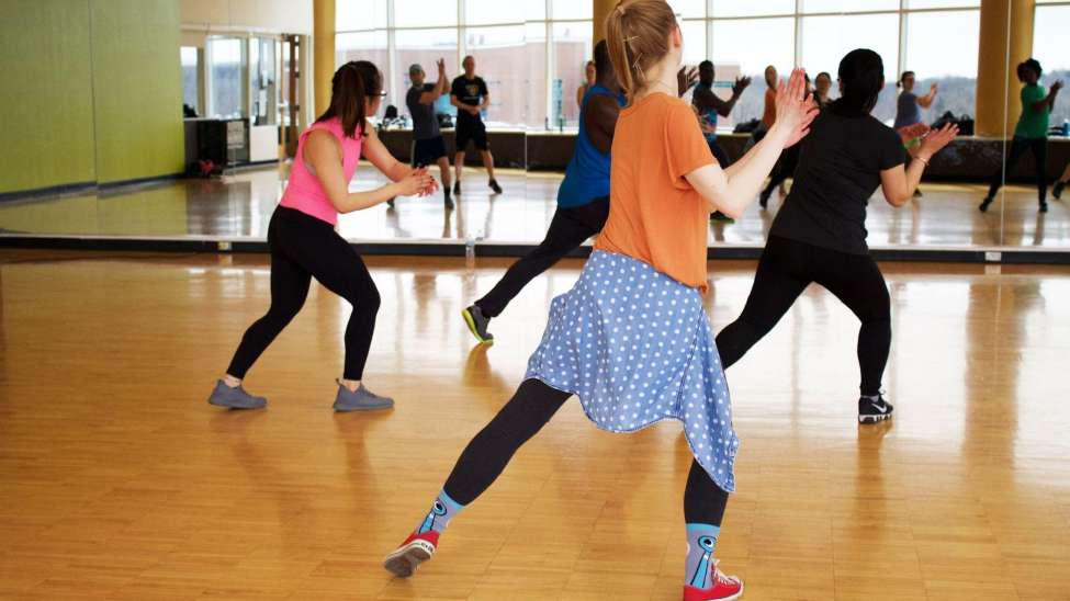 People dancing in a dance glass. They are leaning to the side and clapping and are facing the mirror.