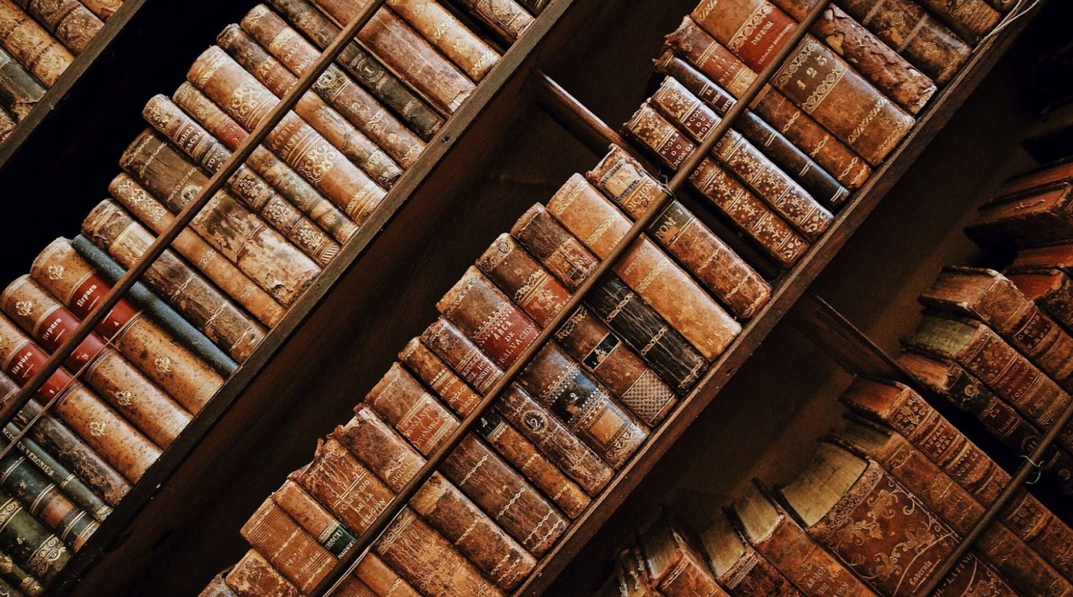 Some old, brown, wooden bookshelves that have old books covering every shelf.