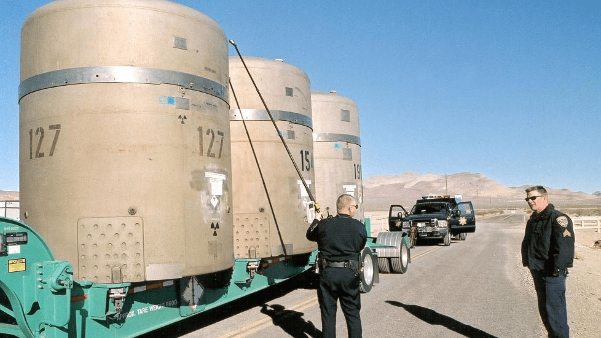 Highway Patrol officers inspect large canisters of radioactive waste on the back of a truck.
