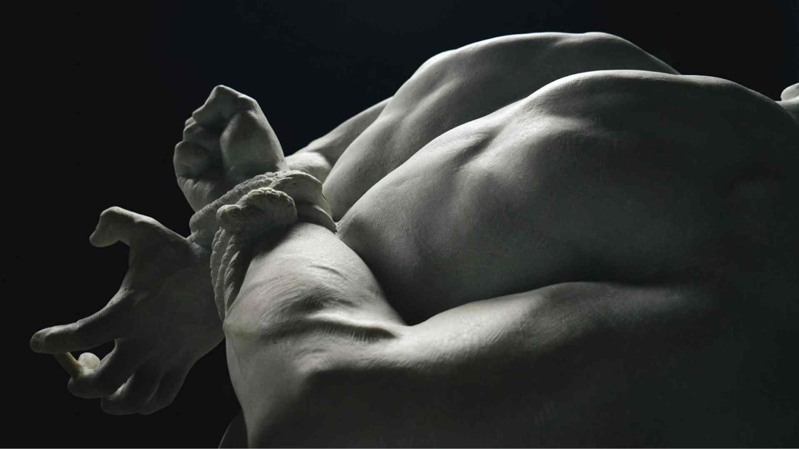 A man has his arms restrained behind his back with a rope.