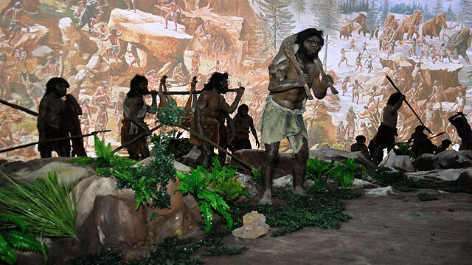 Some figures that showcase human evolution. These are cavemen and they are standing near rocks and green leaves.