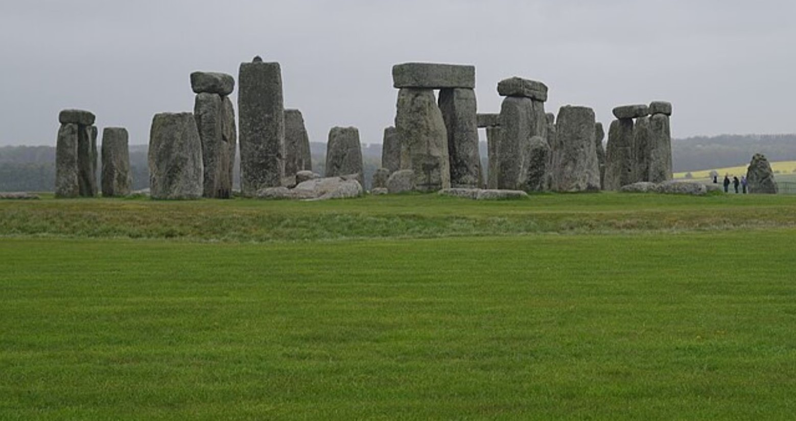 Stonehenge on a cloudy day. Some people are in the background looking at the stones.