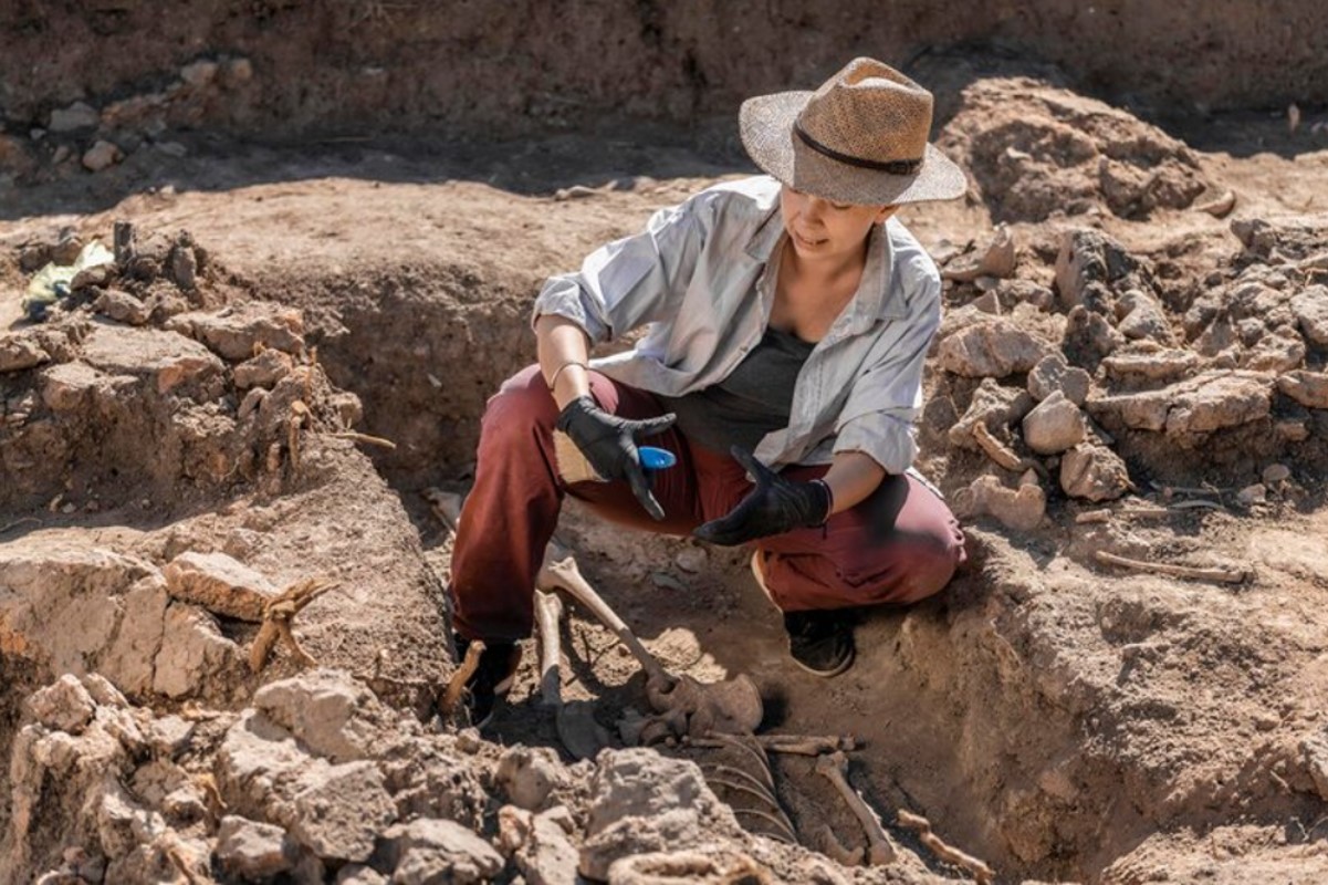 An archaeologist is pictured in a blue shirt as she works at an excavation site
