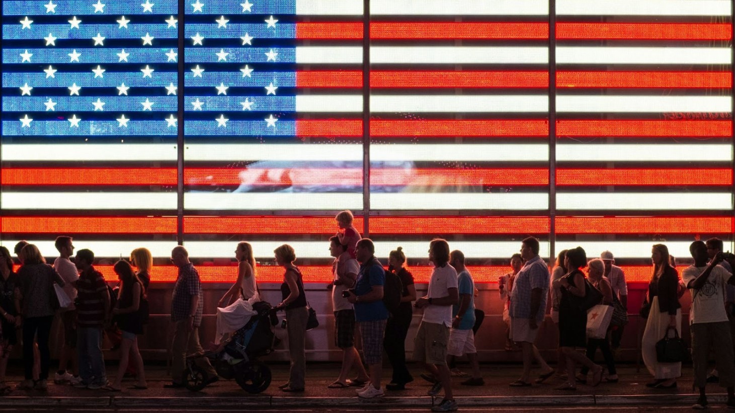 A diverse crowd of people gathered in front of a large, illuminated American flag display