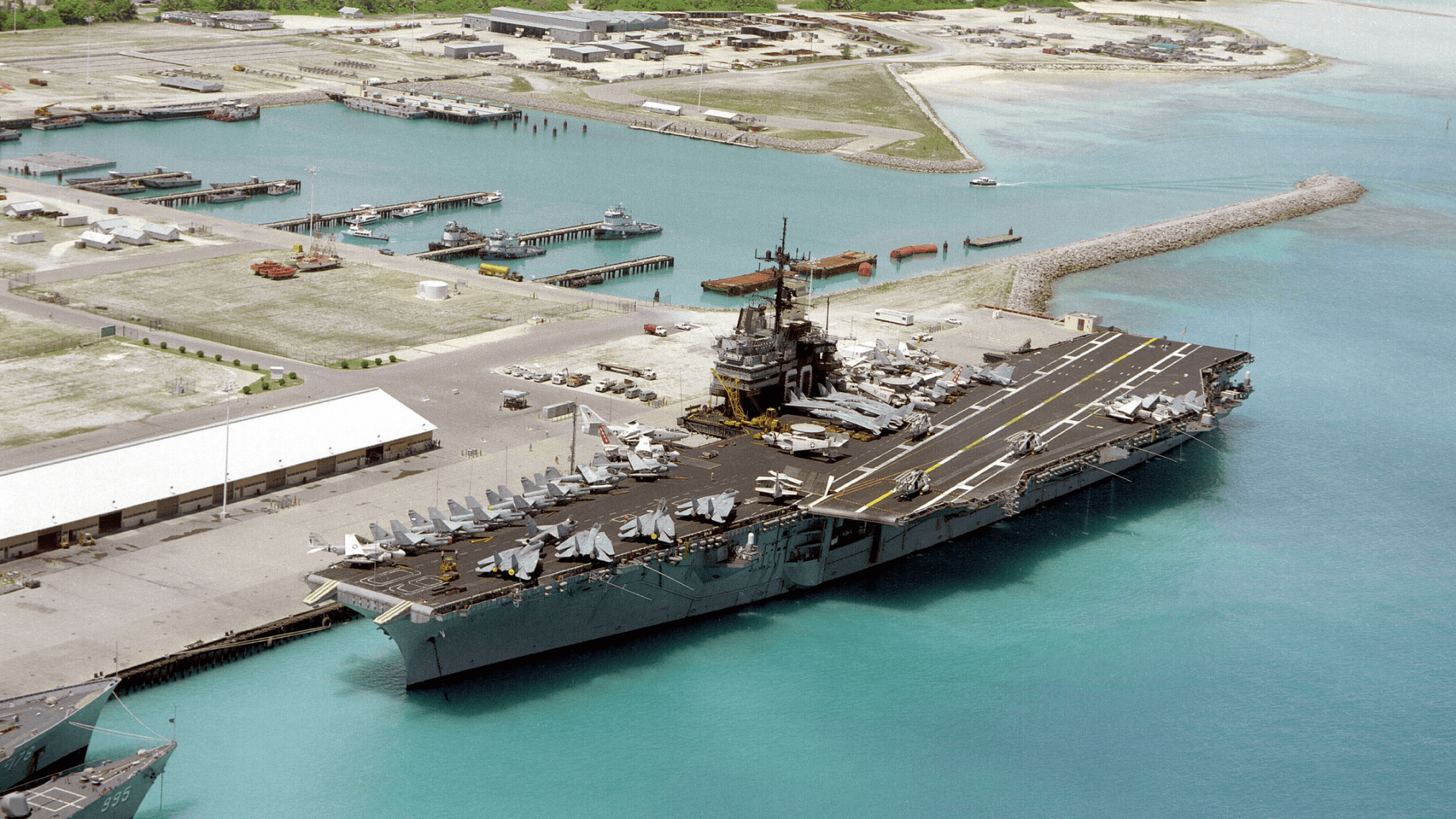 An aerial port bow view of the aircraft carrier USS SARATOGA (CV-60) tied up at pier. This was the first time an aircraft carrier had docked at the island Diego Garcia.