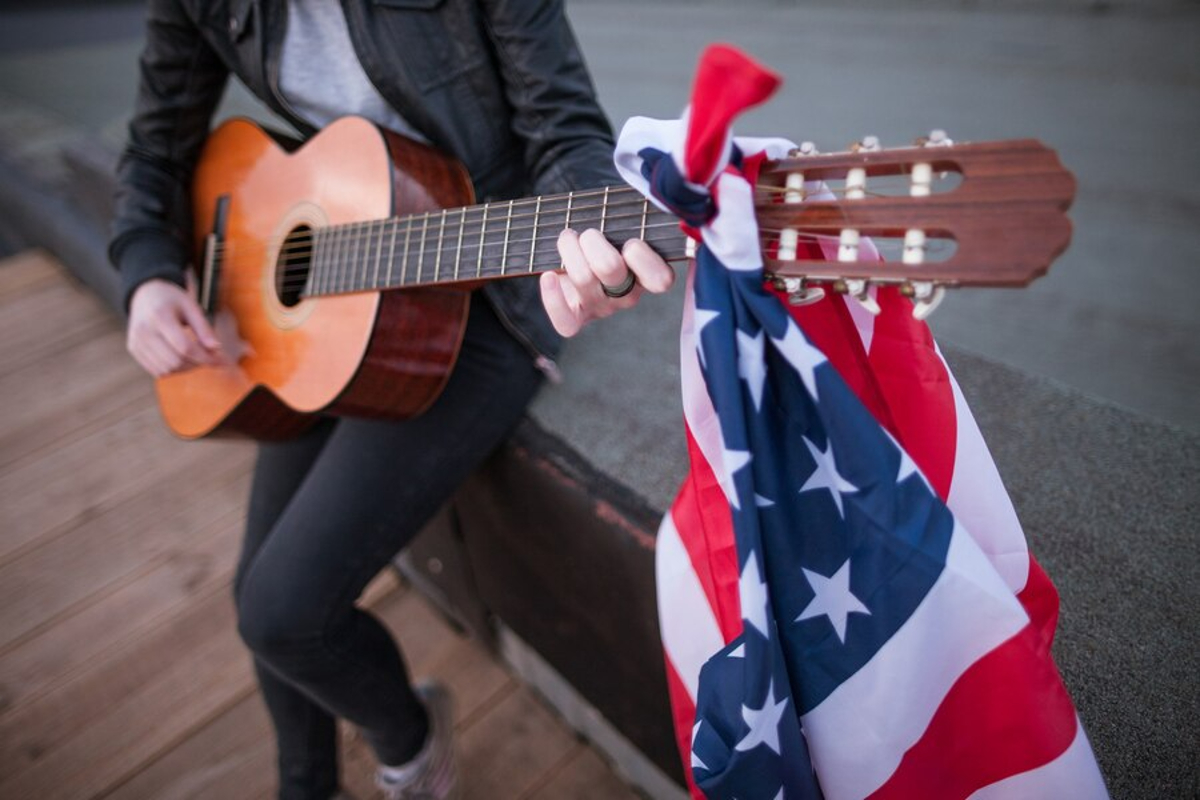 Man in a suit playing a guitar with an American flag tied around the neck