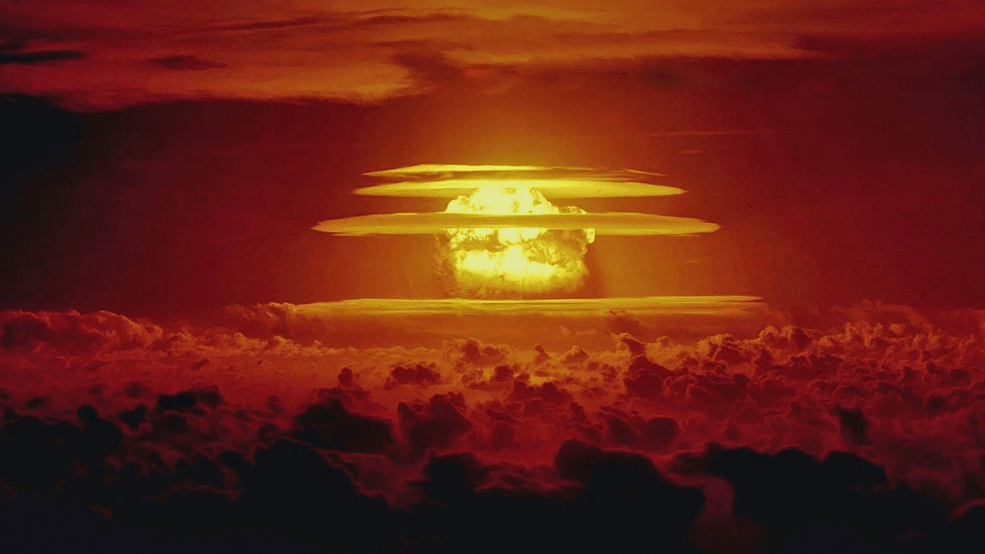 Castle Bravo nuclear test showing a massive explosion with ringed clouds around it in the sky above cloud cover.