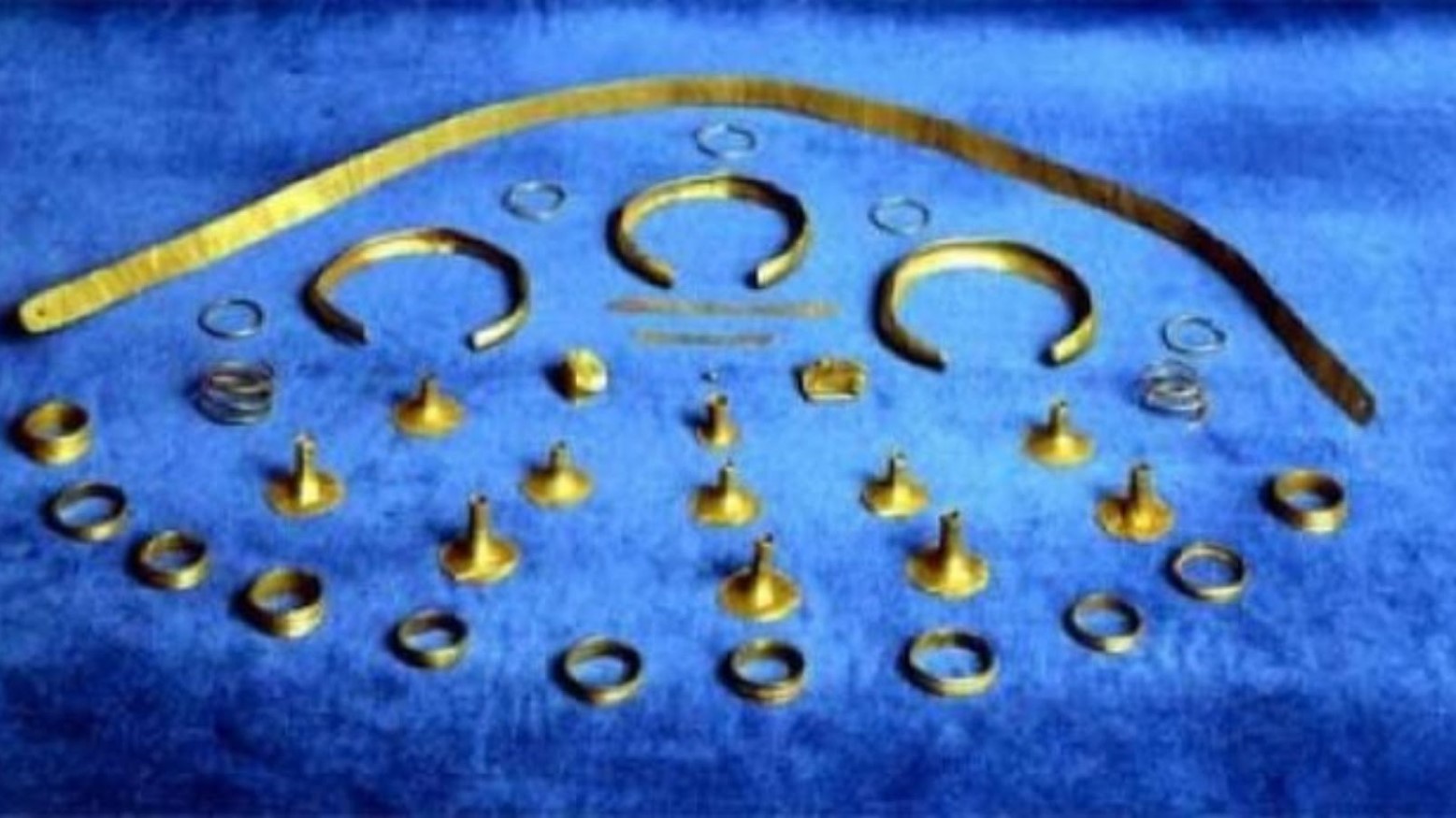 The Treasure of Cabezo Redondo against a blue background. The findings are quite small and look like small rings, bracelets, and a gold band.