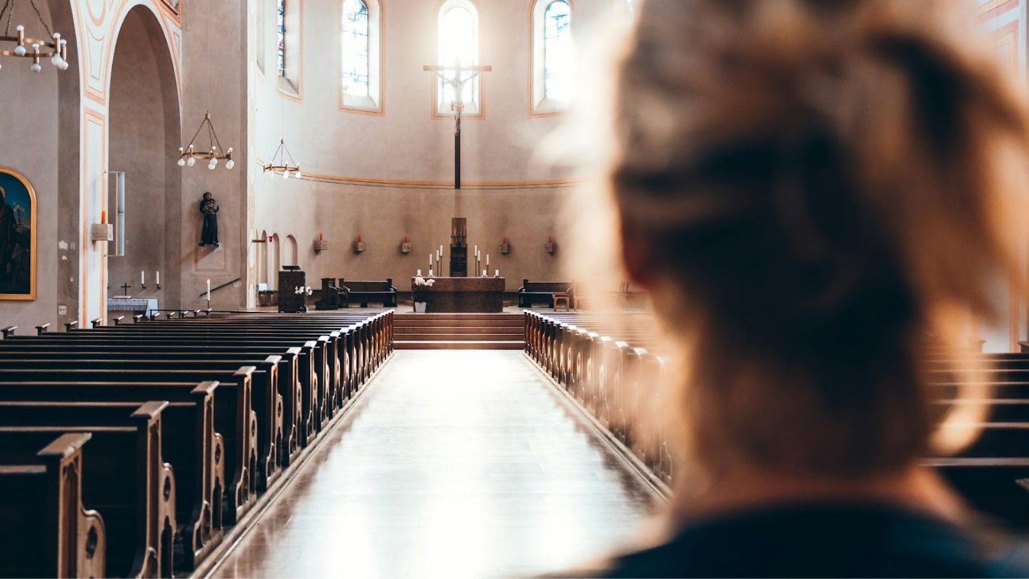 The photograph is taken from behind a person whose blurred silhouette frames the image, gazing down the central aisle of a church