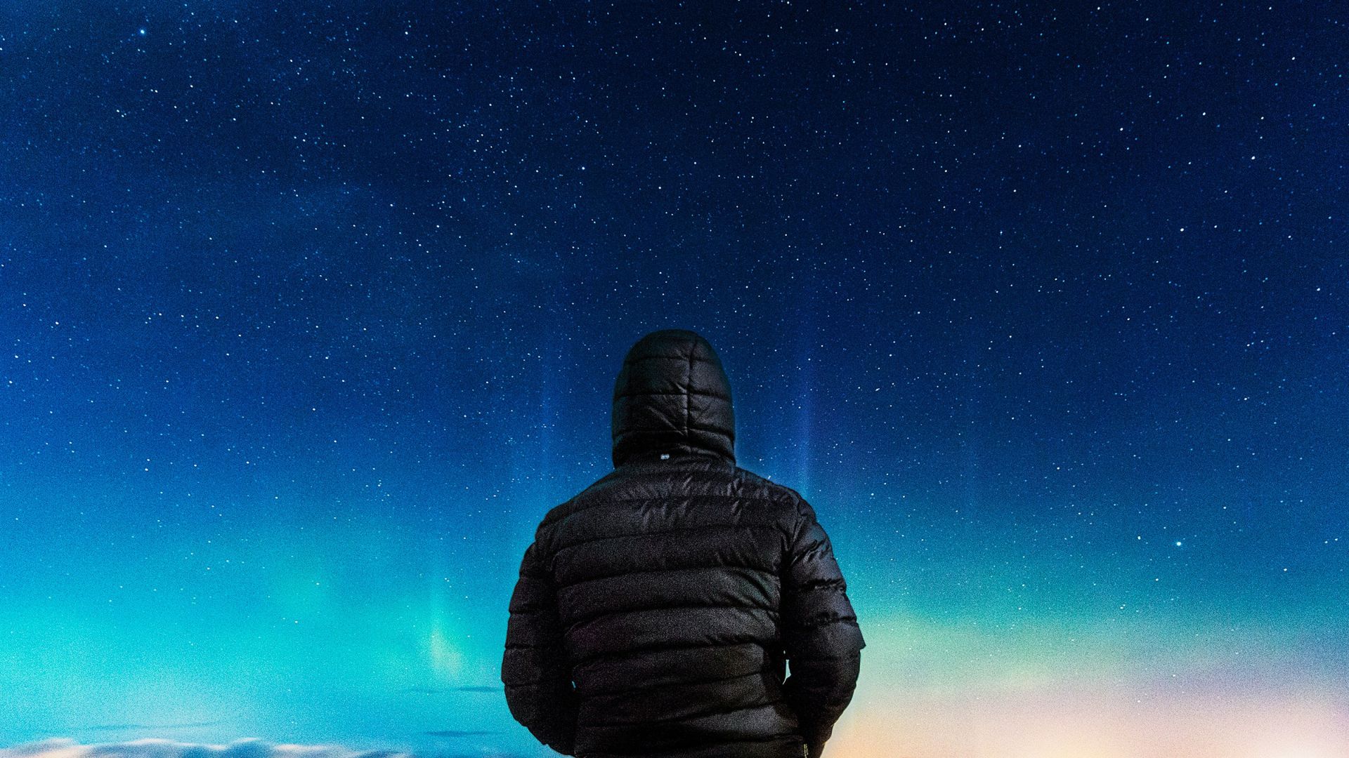 A man in a black jacket stands before a very starry sky.