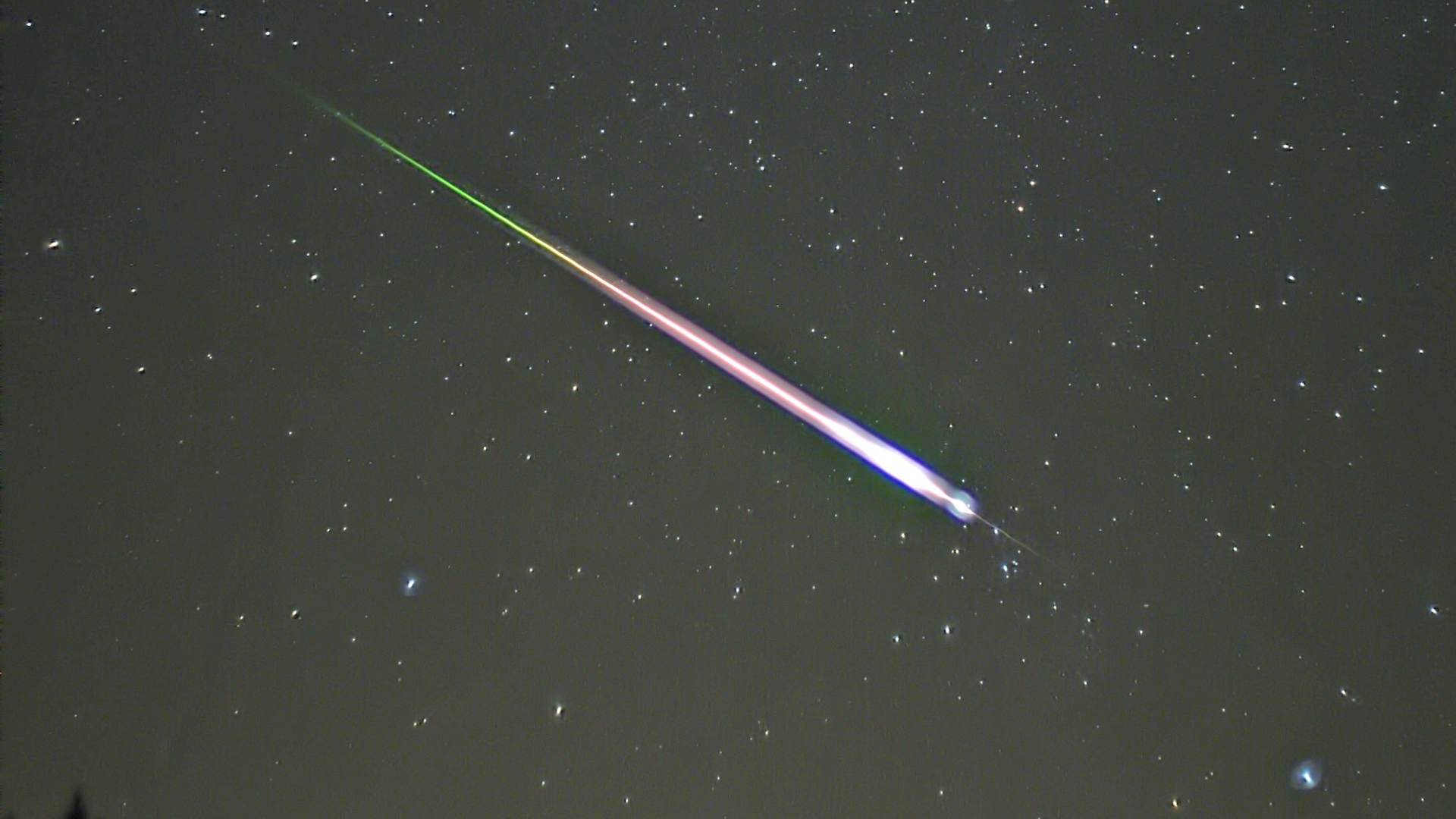 A meteor falls in the night sky.