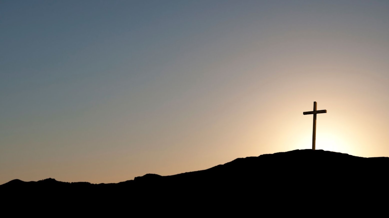 A large cross sits on a hill as the sun rises