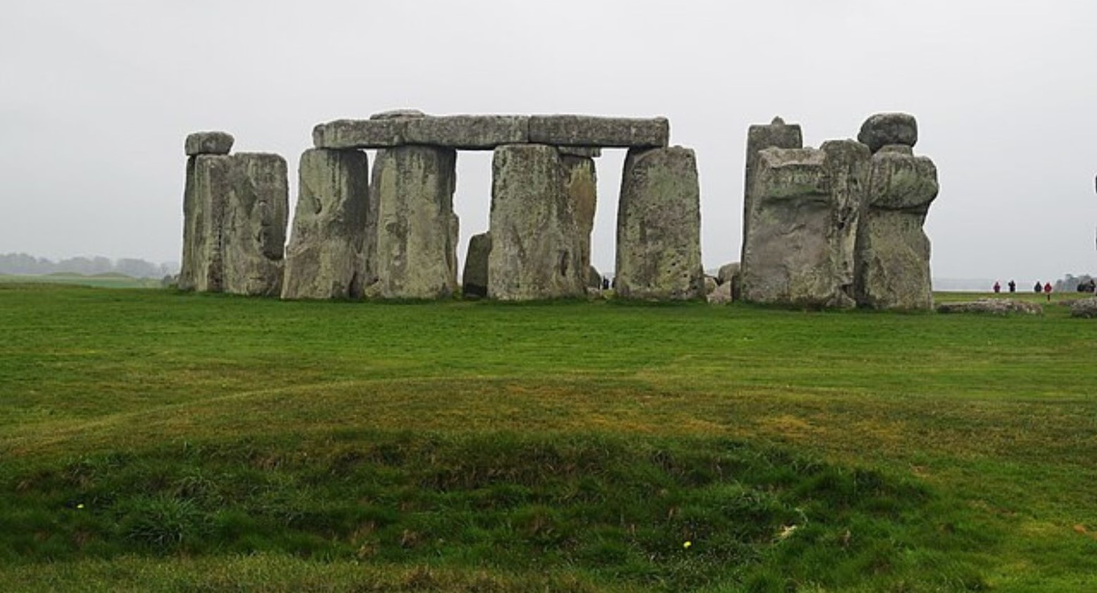 Stonehenge from a distance on a cloudy day. Some people can be seen in the distance looking at the stones.