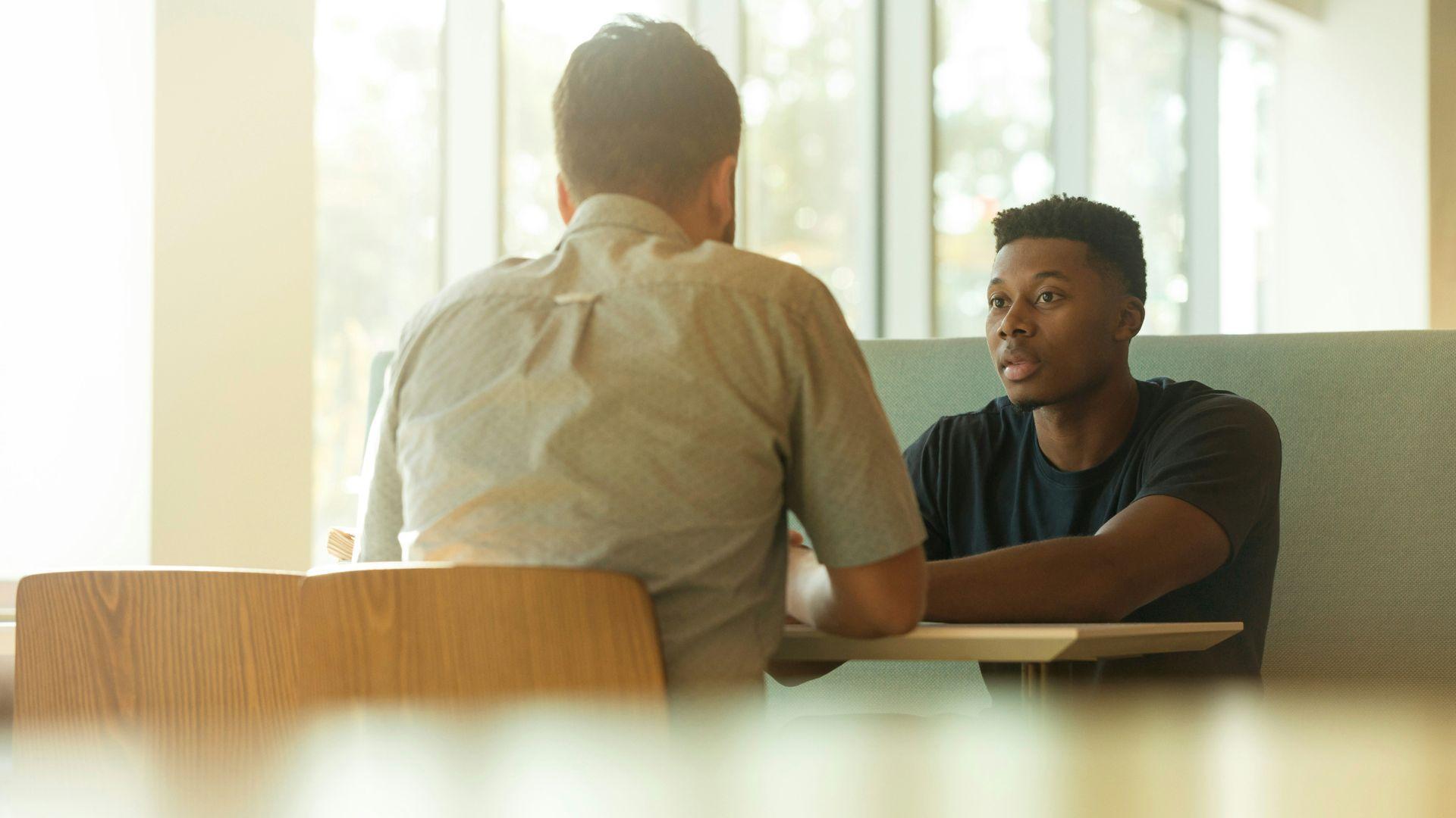 Two men sitting down at a table and talking.