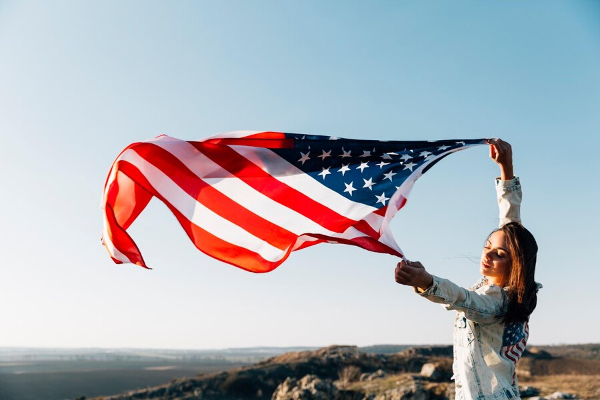 A woman holds an American flag in the wind on a cliff