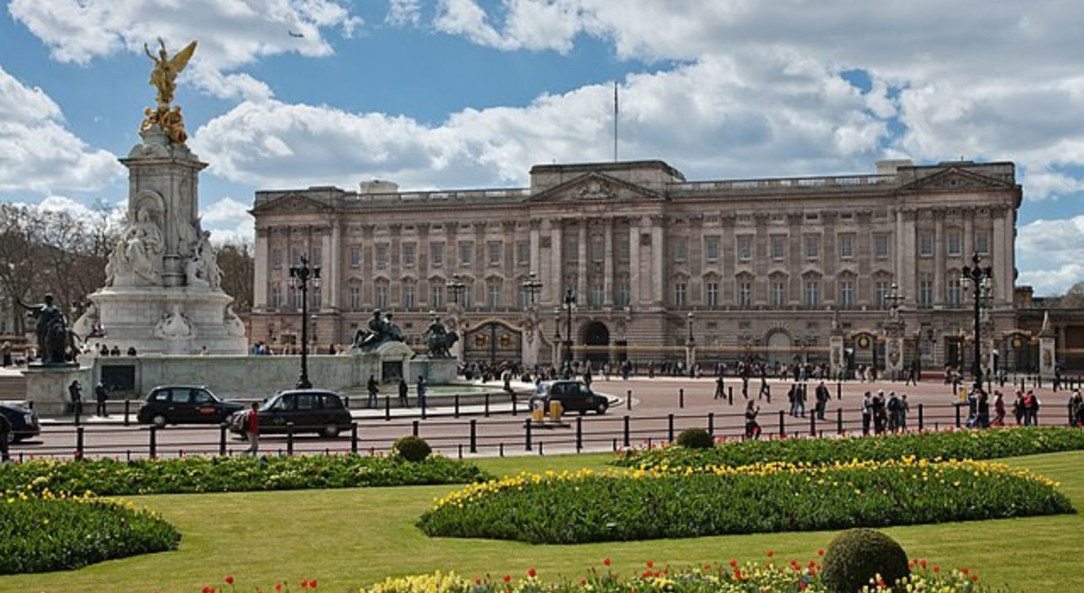 A view of Buckingham Palace from the Mall, which is where King Charles (the crown) lives. The Queen Victoria monument can be seen from the center of the mall, outside Buckingham Palace.