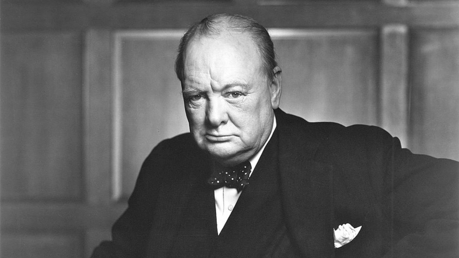 Black and white portrait of Winston Churchill. The former British Prime Minister is depicted in a dark suit with a polka-dot bow tie and a white pocket square