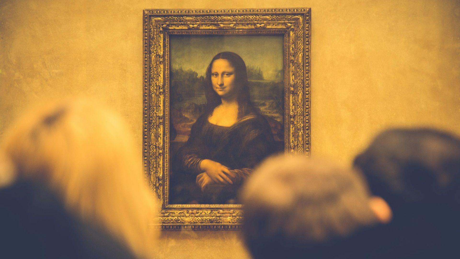 People standing in front of the framed Mona Lisa on a wall.