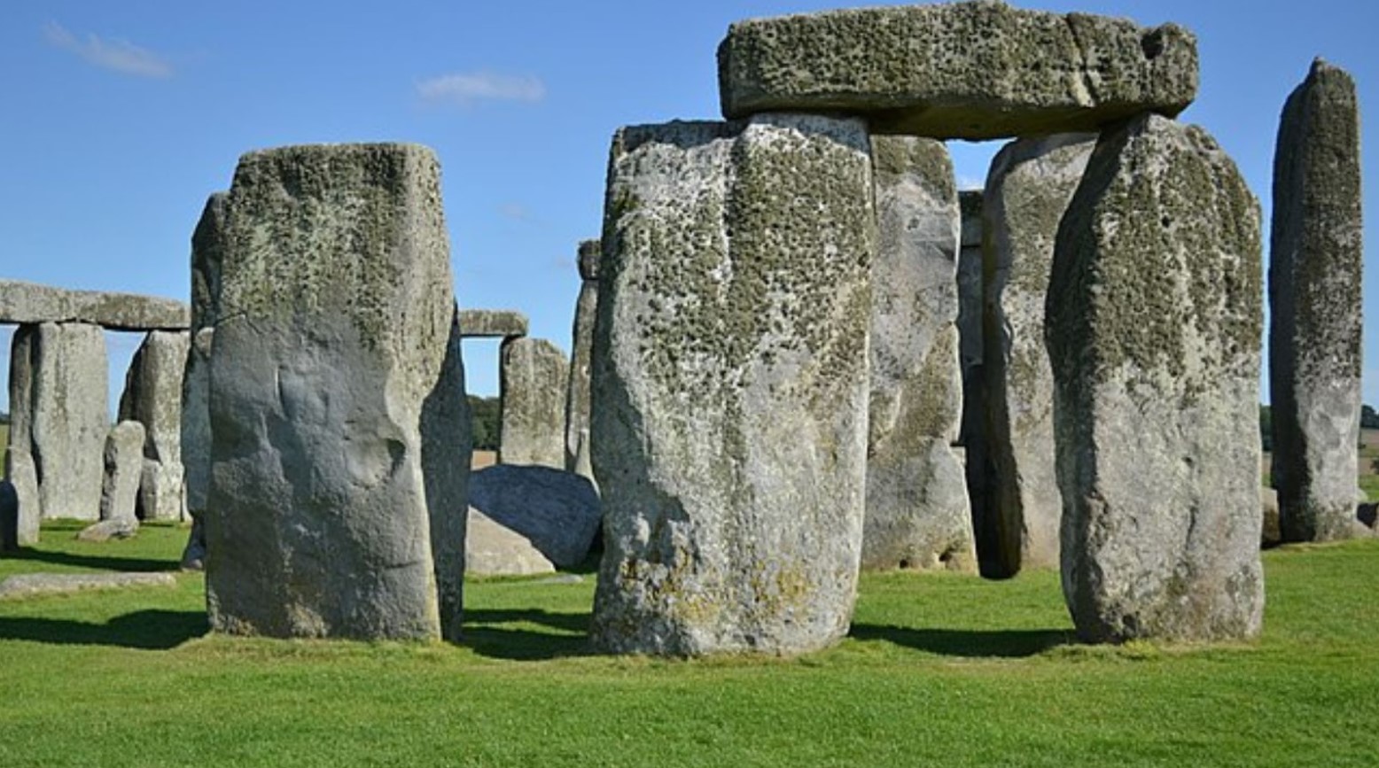 A close-up of Stonehenge on a sunny day. Some of the stones are on top of each other, whereas others stand alone. There is moss on the top parts of each stone.