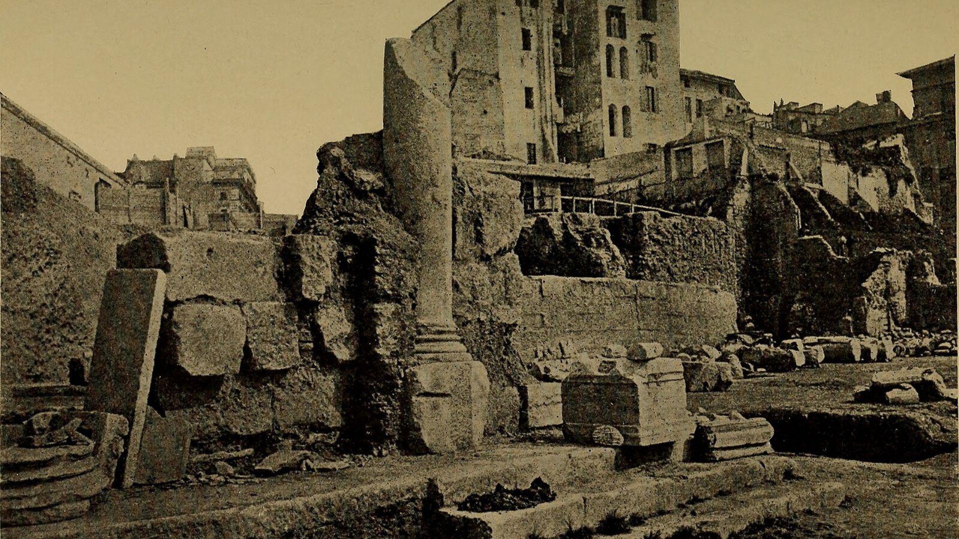 Sepia-toned photograph of the ancient Roman Forum ruins. Visible are the remnants of several columns and arches, with large blocks of stone strewn across the ground. In the background, modern buildings loom directly above the ruins