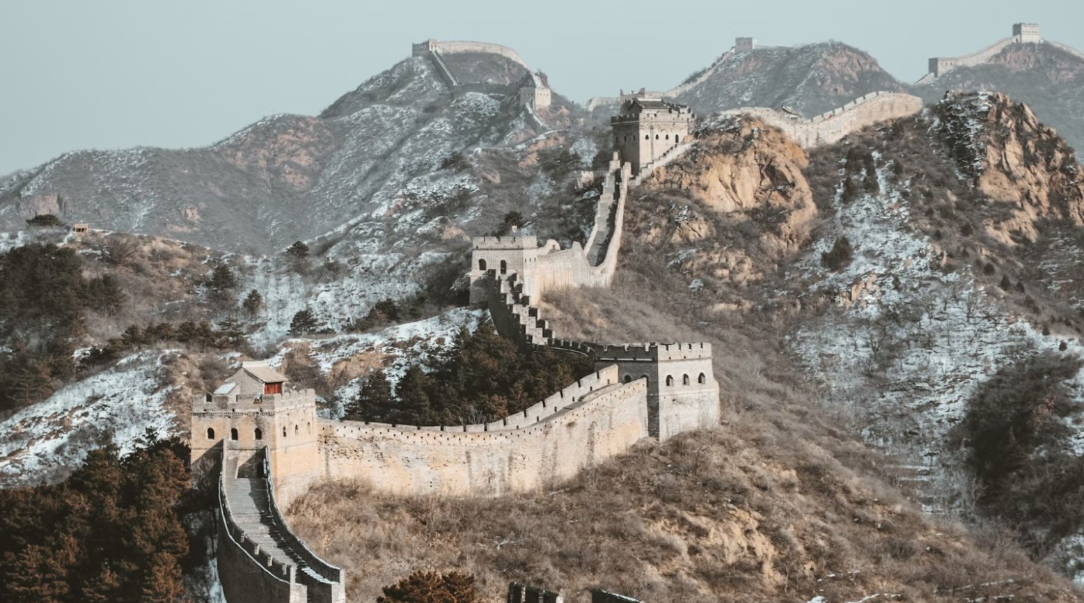 The Great Wall of China during winter. There is some snow on parts of the hills. The wall follows the hills up and around.