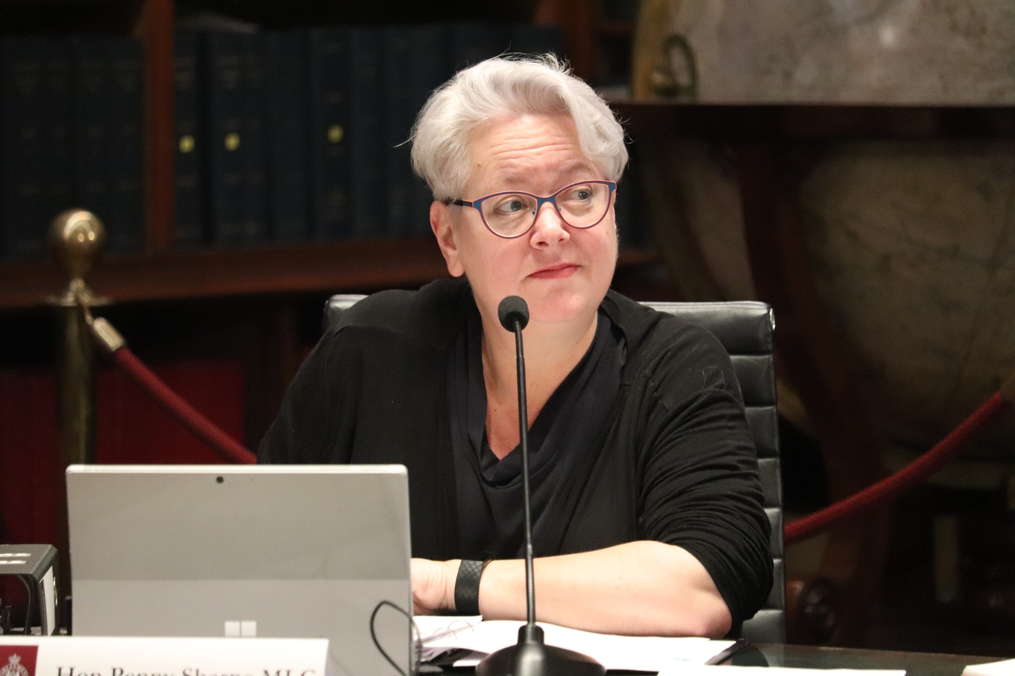 A woman with short grey hair and a black button up sitting in front of a microphone