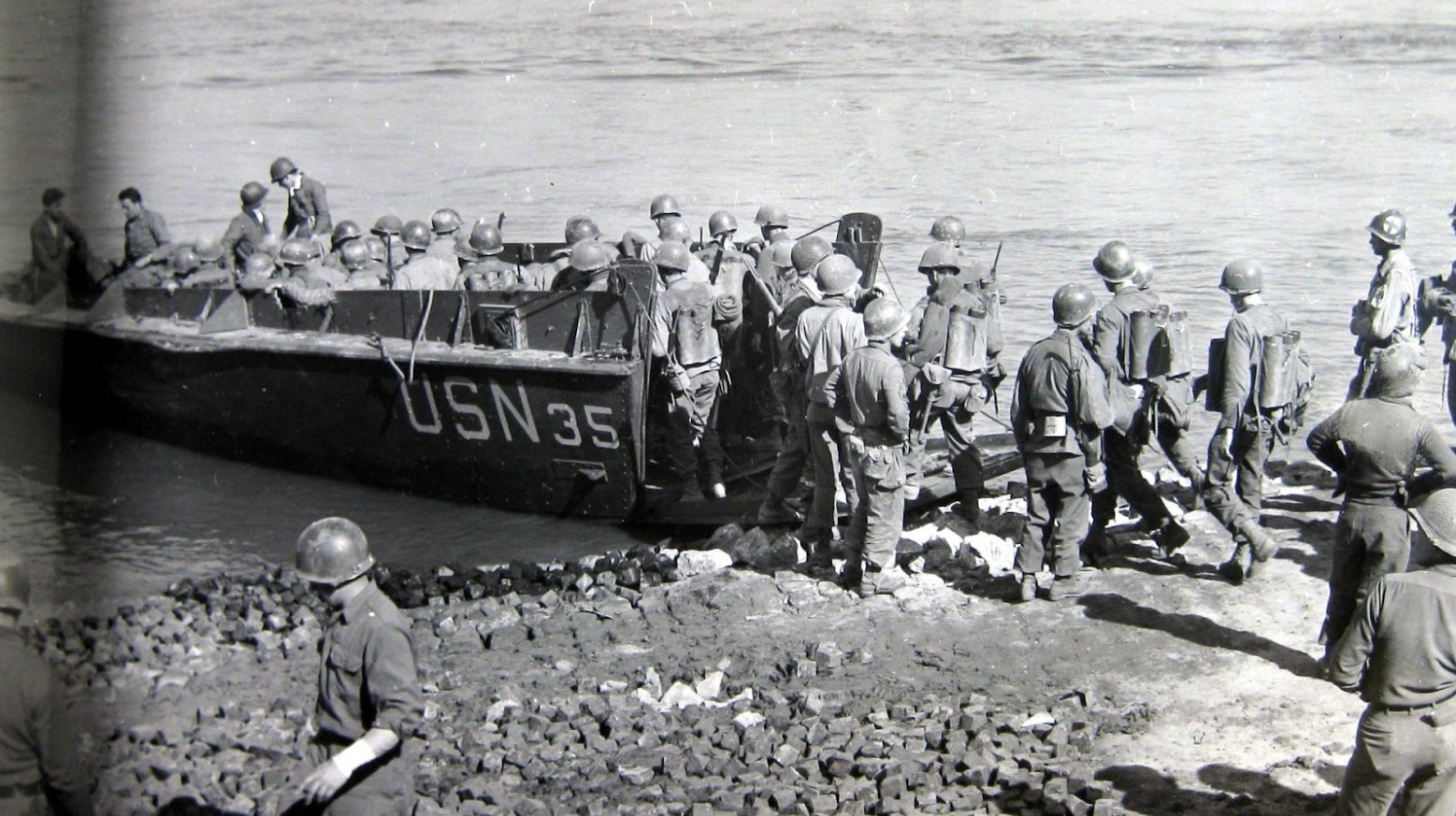 A black and white image of American soldiers loading onto a boat to cross the Rhine River in Germany during World War II.