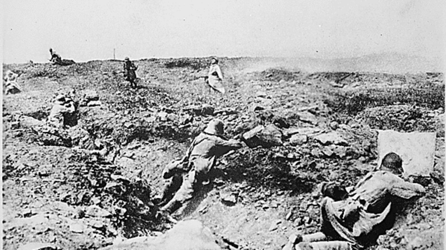 A grainy black and white photograph capturing World War I soldiers in a rugged battlefield setting