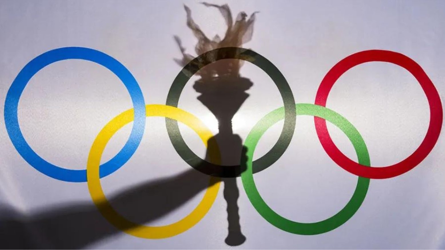 Silhouette of a hand holding a torch behind a flag for the Olympic Games