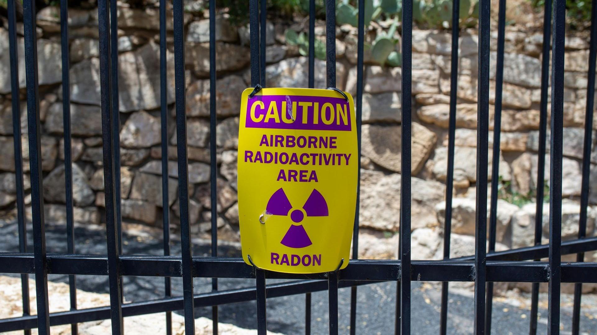A Caution sign warning of Airborne Radioactivity on a steel fence.