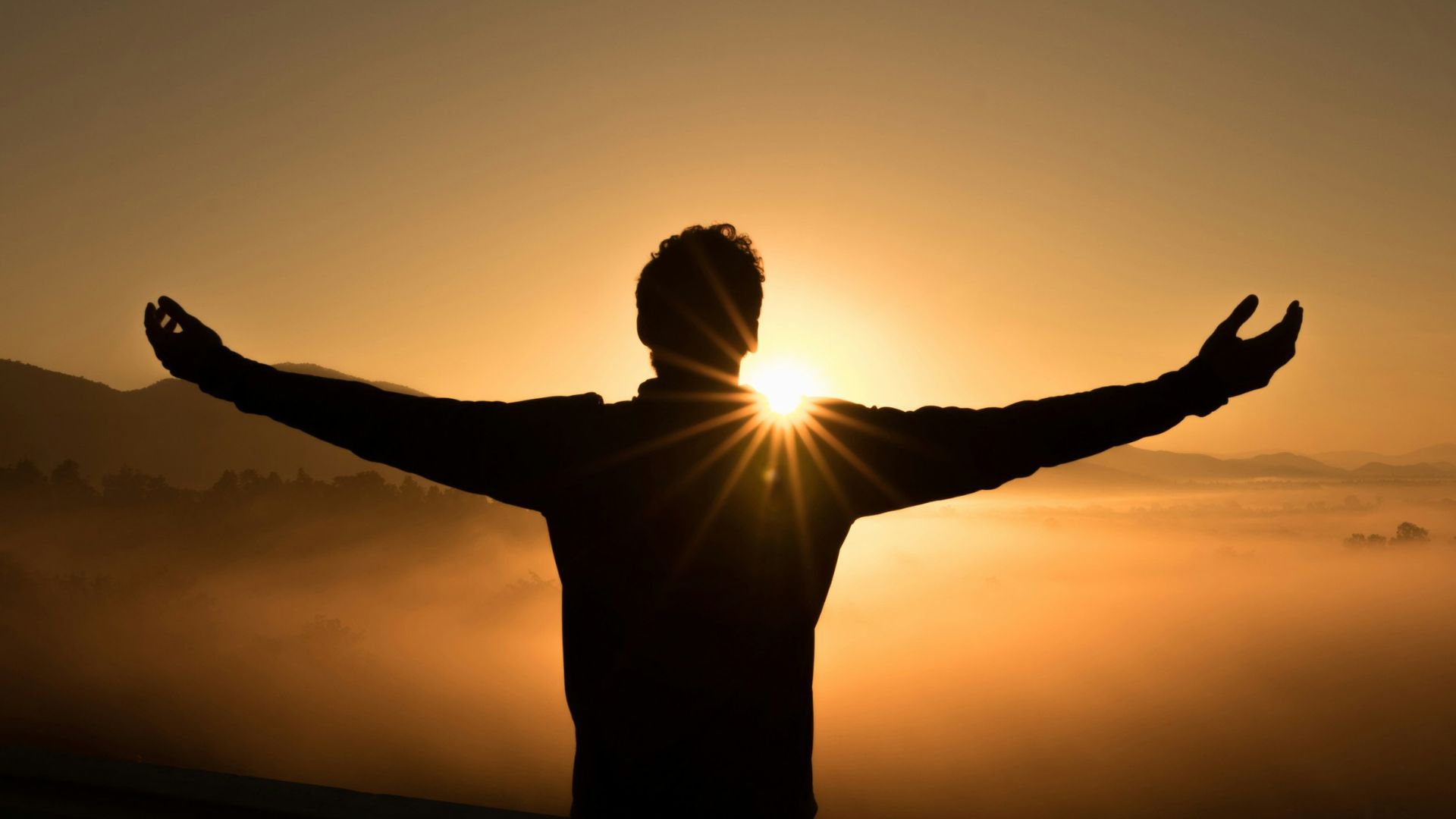 The silhouette of a person raising their open arms during a sunset.