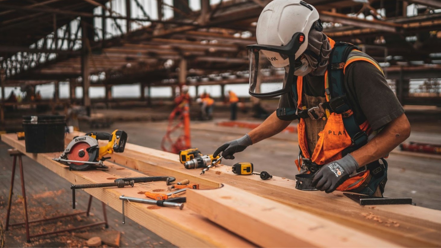 A construction worker wearing protective gear is using a circular saw to cut a piece of wood on a workbench