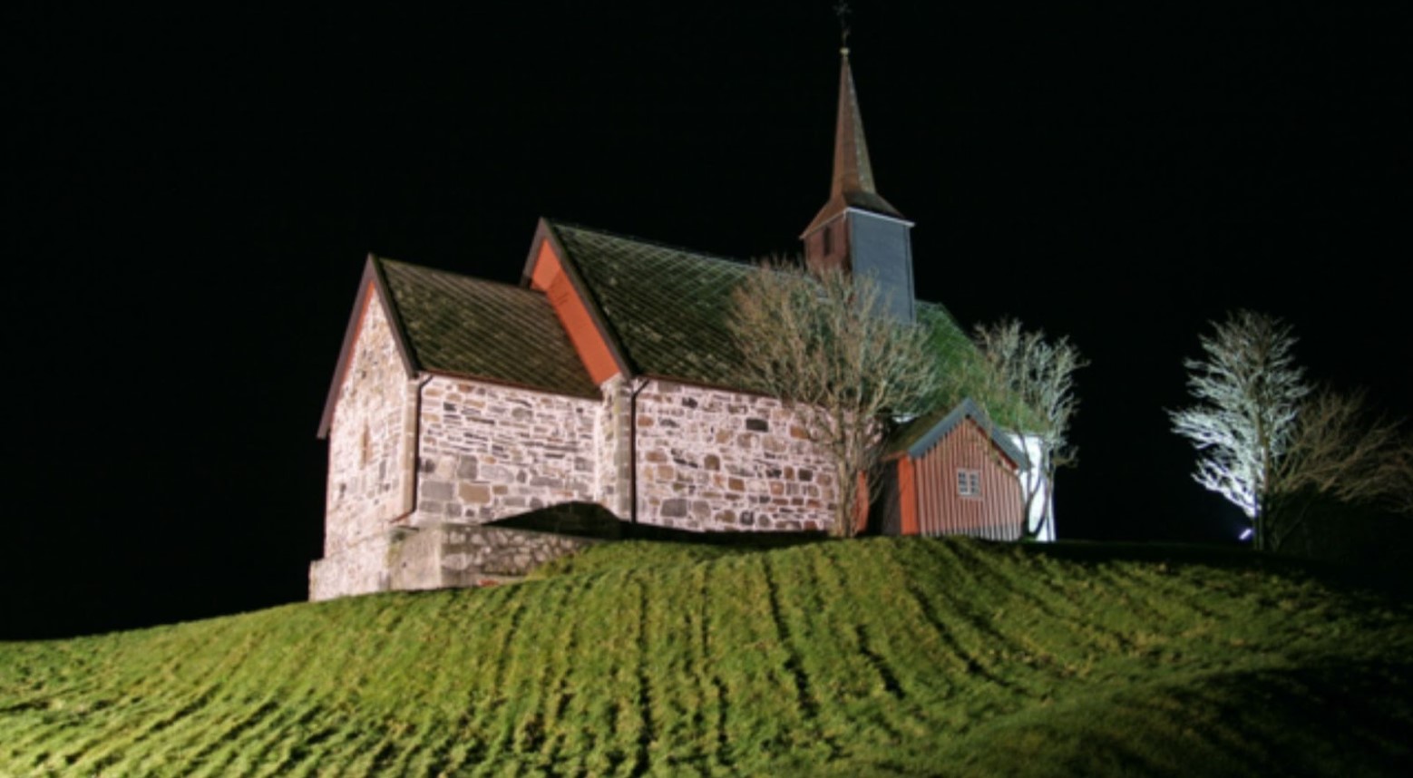 Edoy Church at night. The Church is on a grassy hill and is surrounded by trees.