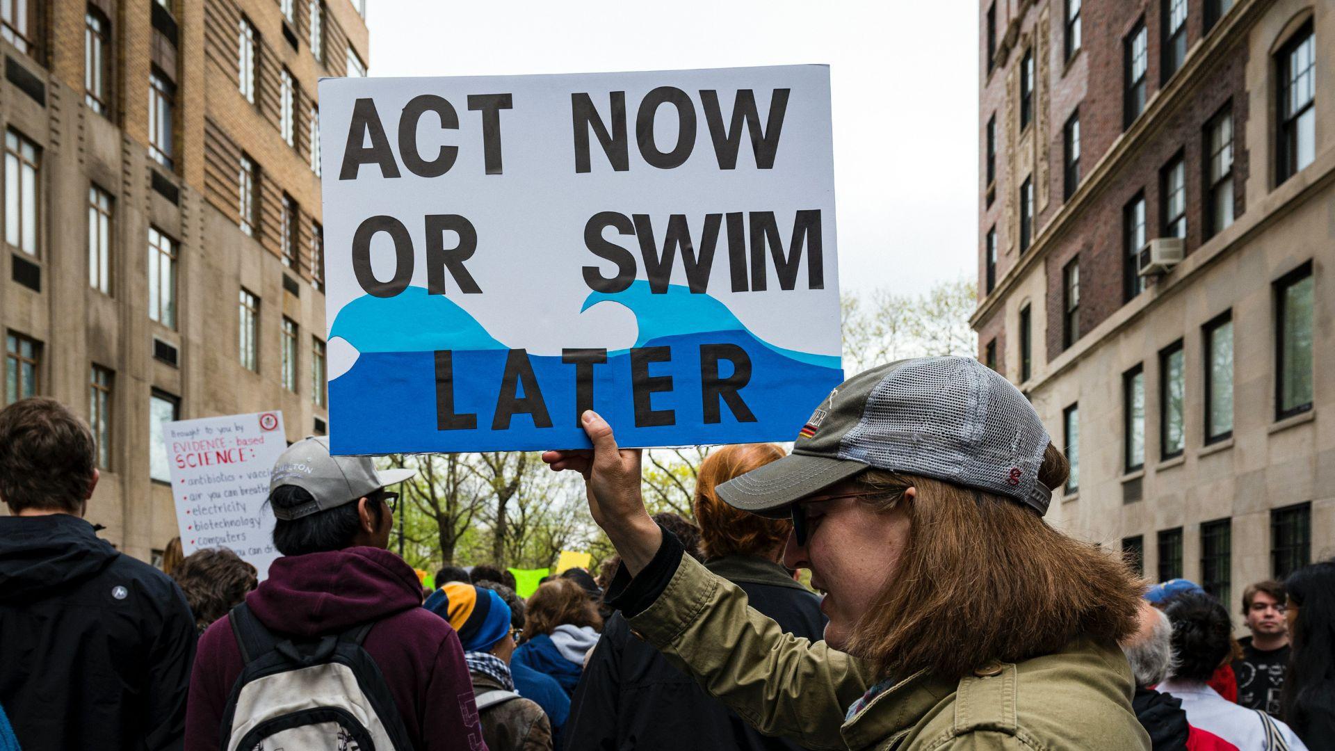 A protestor holding a climate change sign while outside with others in a rally.