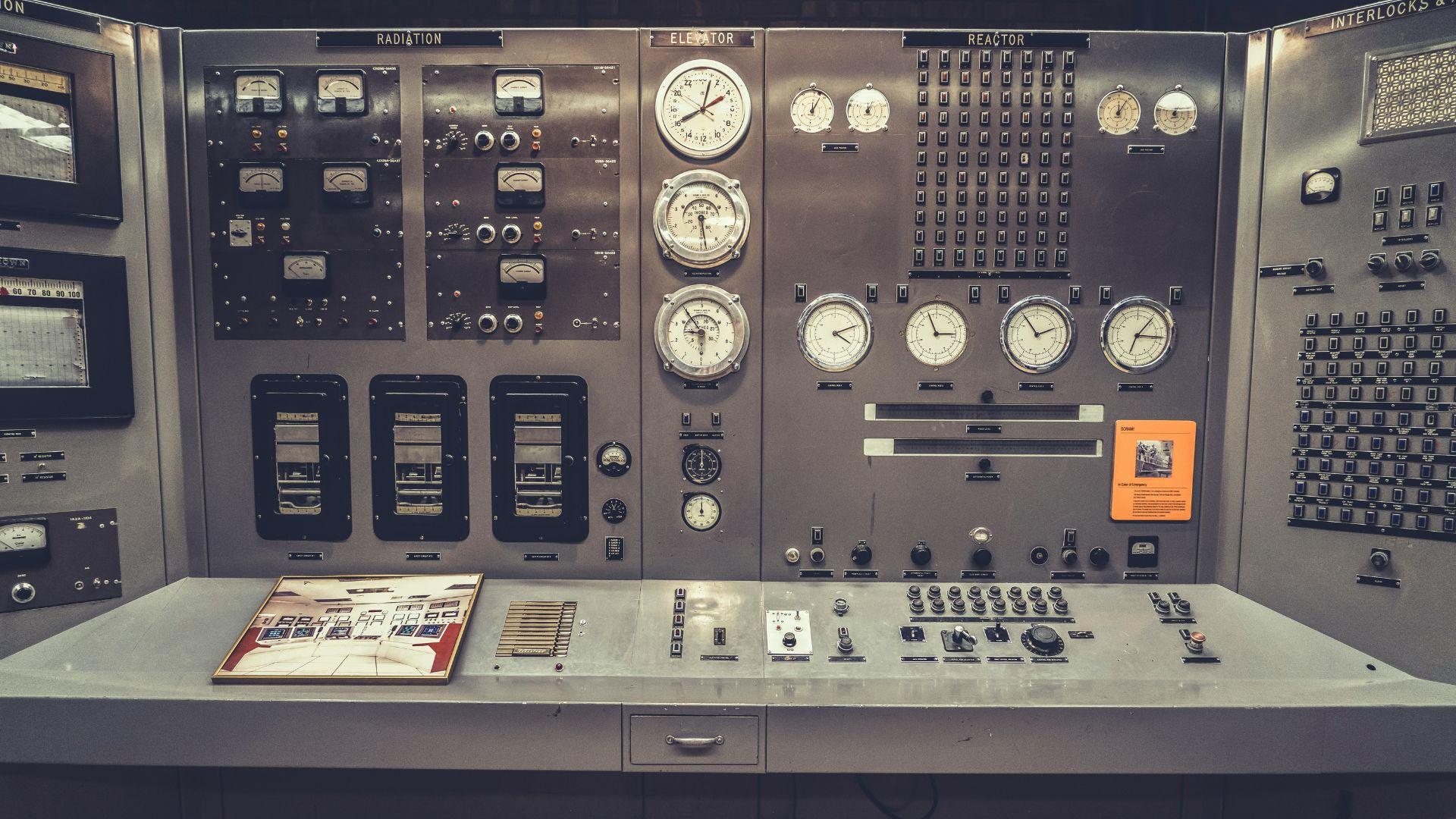 A photo of an old nuclear power plant control room, which is all gray with many meters and buttons.