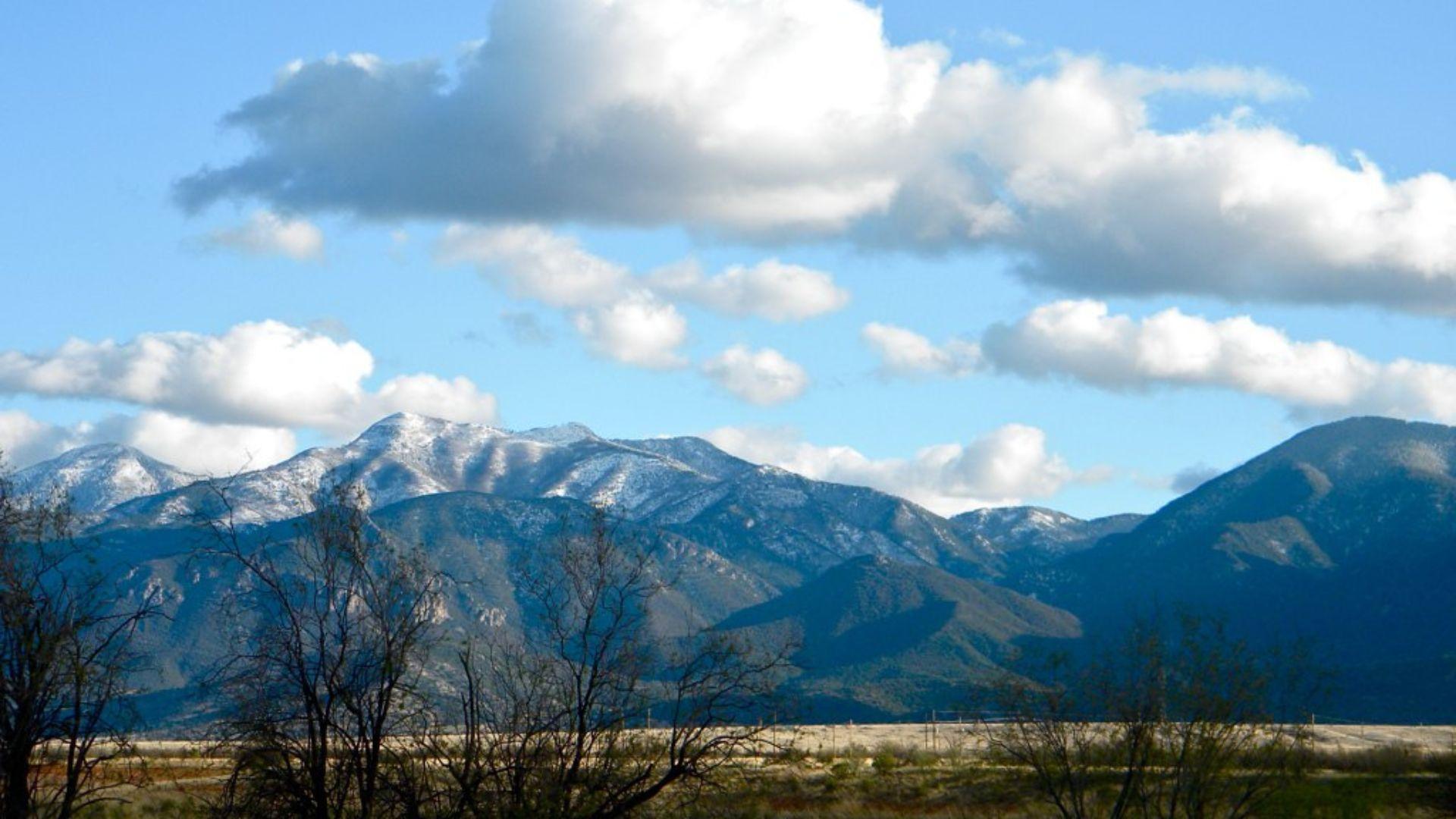 A vivid landscape showcasing a range of snow-capped mountains under a bright blue sky scattered with fluffy white clouds